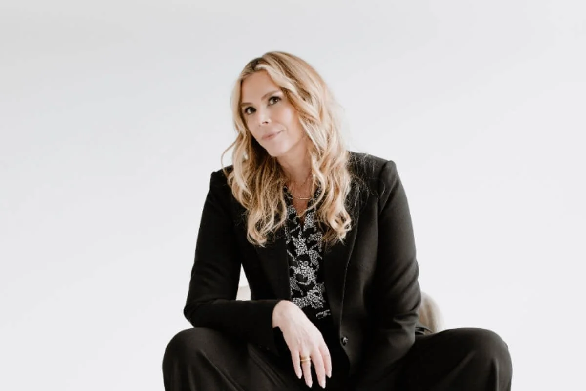 Dr. Kenna in a black suit with a floral blouse sitting against a plain light backdrop, looking at the camera.