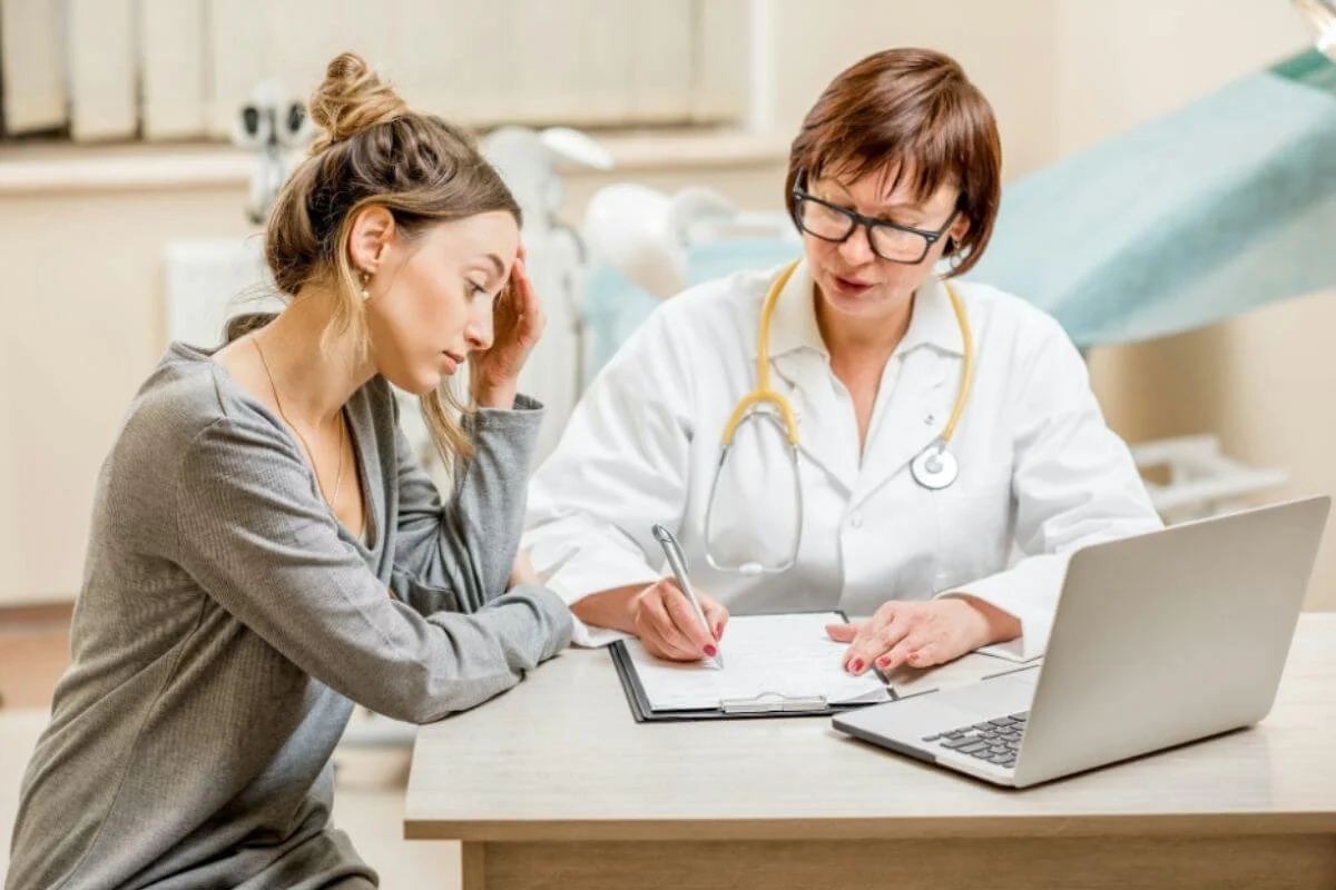 Woman experiencing fatigue and headache during a doctor's appointment, symptoms often dismissed in women's healthcare