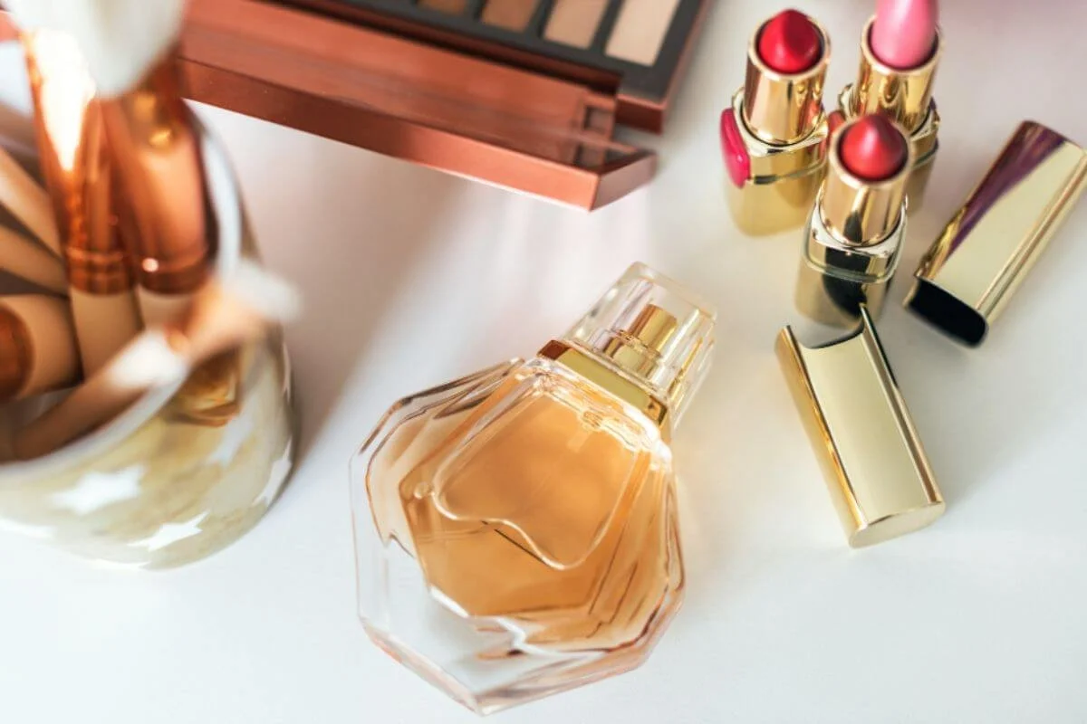 Perfume bottle and gold lipsticks arranged on a vanity next to an eyeshadow palette