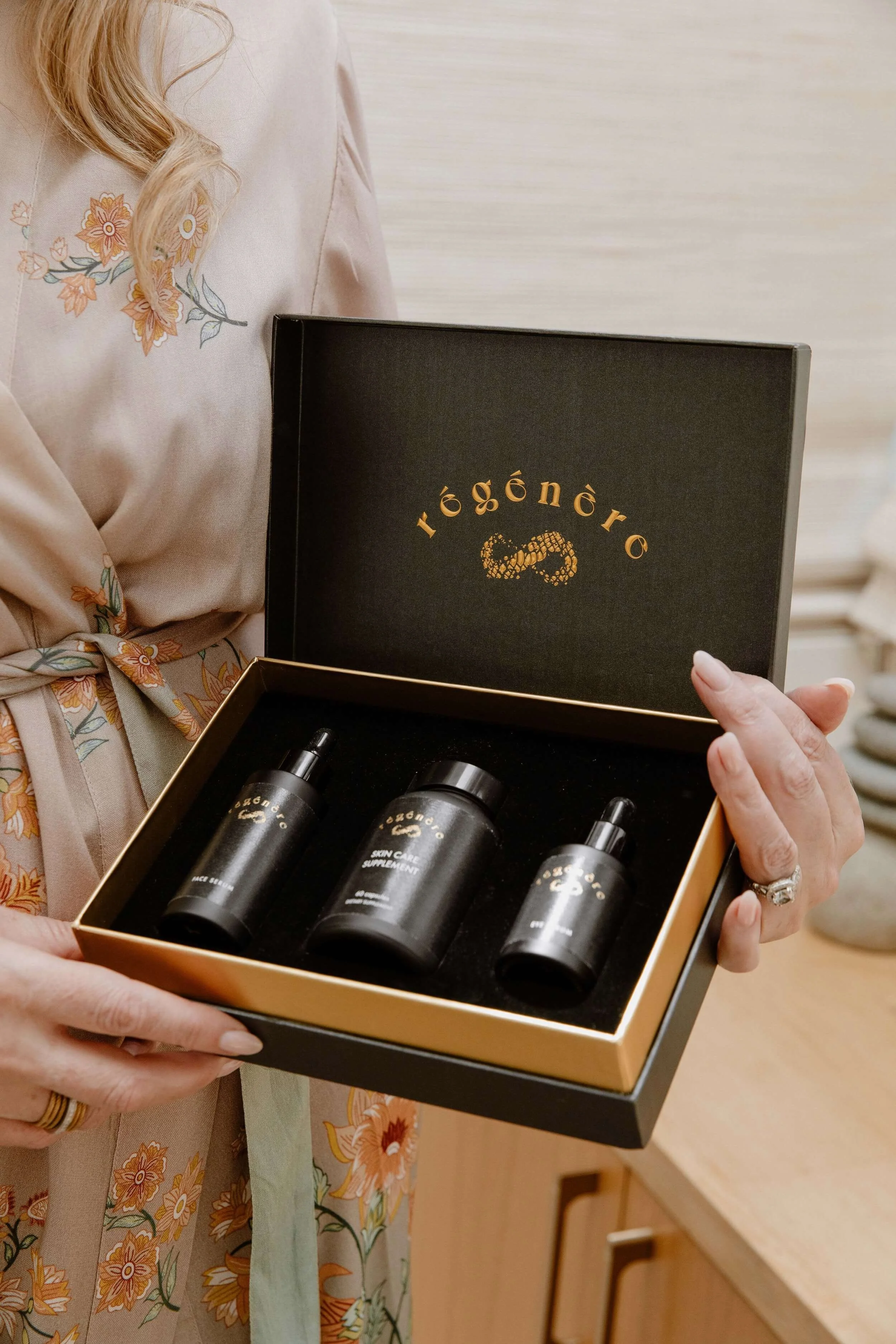 A woman holding an open black and gold box containing skincare products, with the brand name Régénère.