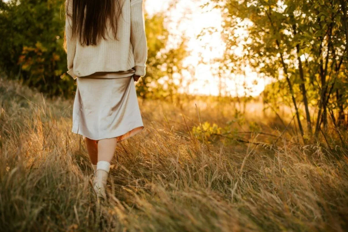 Woman walking through the grass towards the sunset