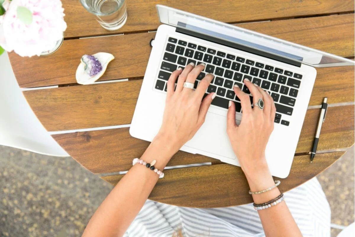 Overhead view of a woman's hands typing on a laptop at a small outdoor table