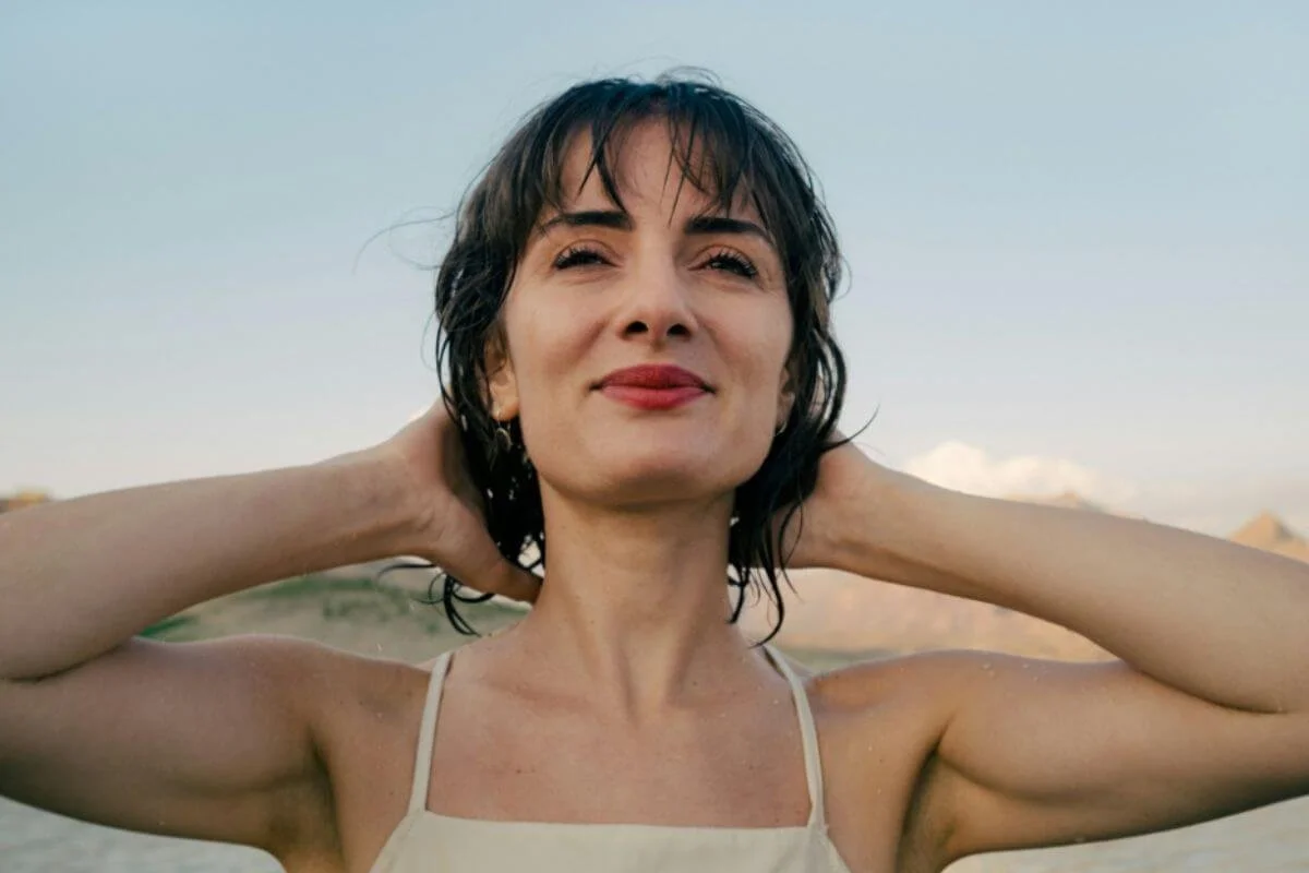 A woman smiling while combing her hair backwards