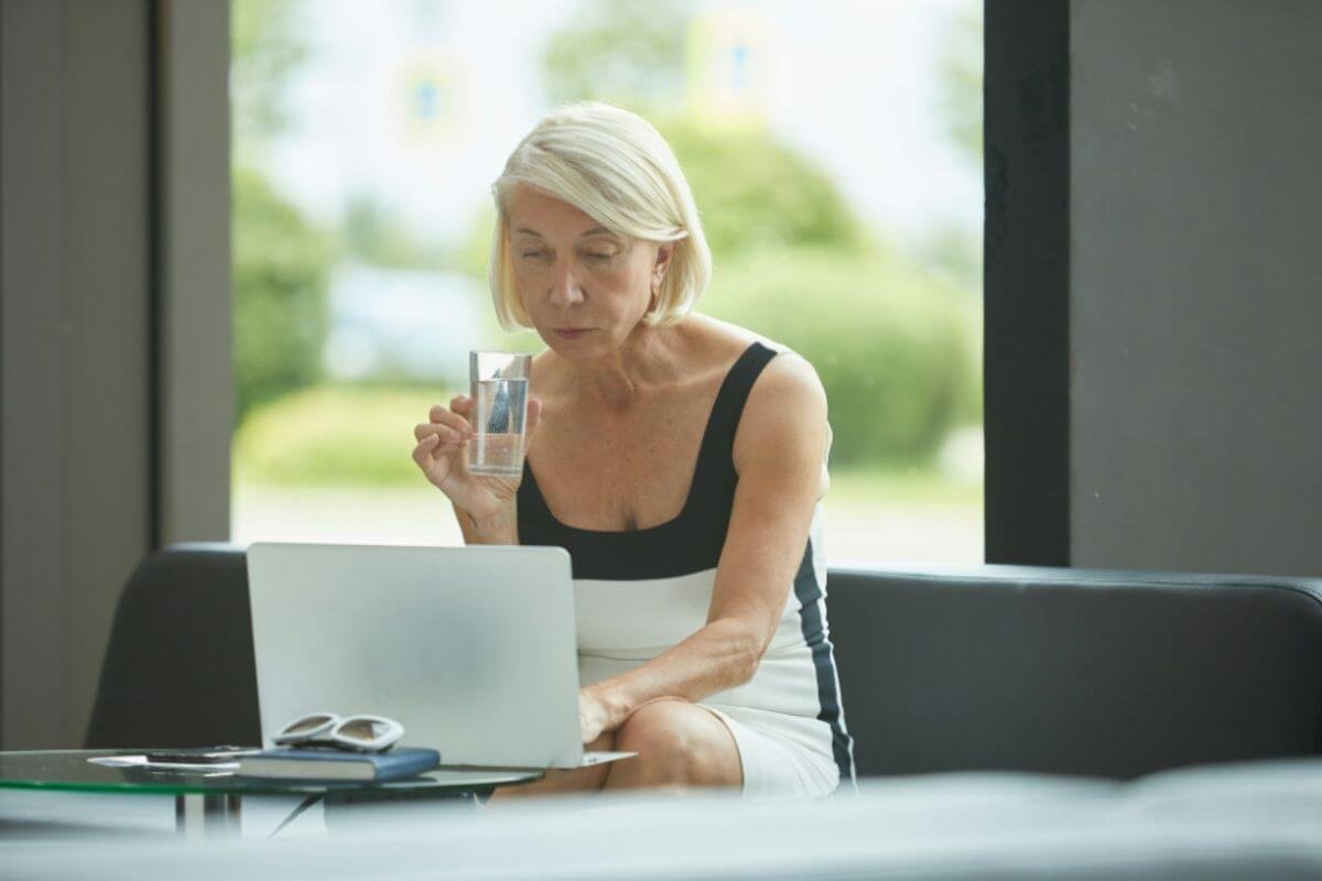 Woman in her 60s in her laptop holding a glass of water