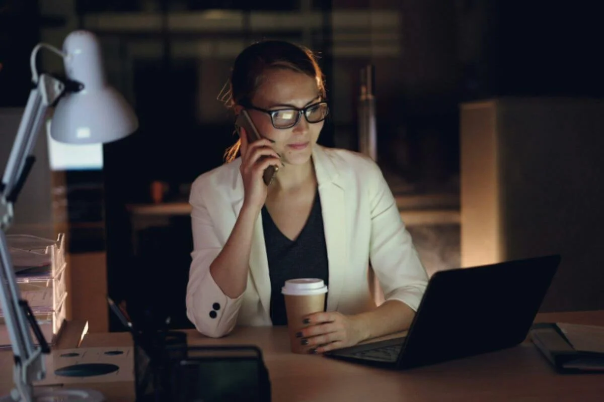 Businesswoman working late on a phone call while reviewing her laptop, illustrating the high-output pace that masks hormonal imbalance symptoms
