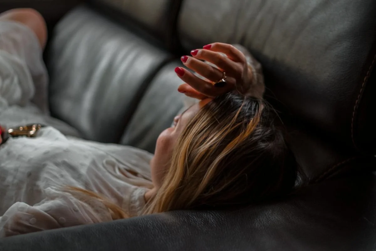 Woman lying on her couch after a trip, eyes closed with her hand pressed to her forehead.