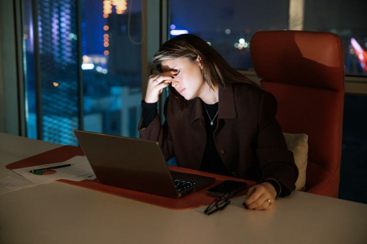 High-performing woman rubbing her forehead at her desk late at night, showing signs of mental fatigue and brain fog
