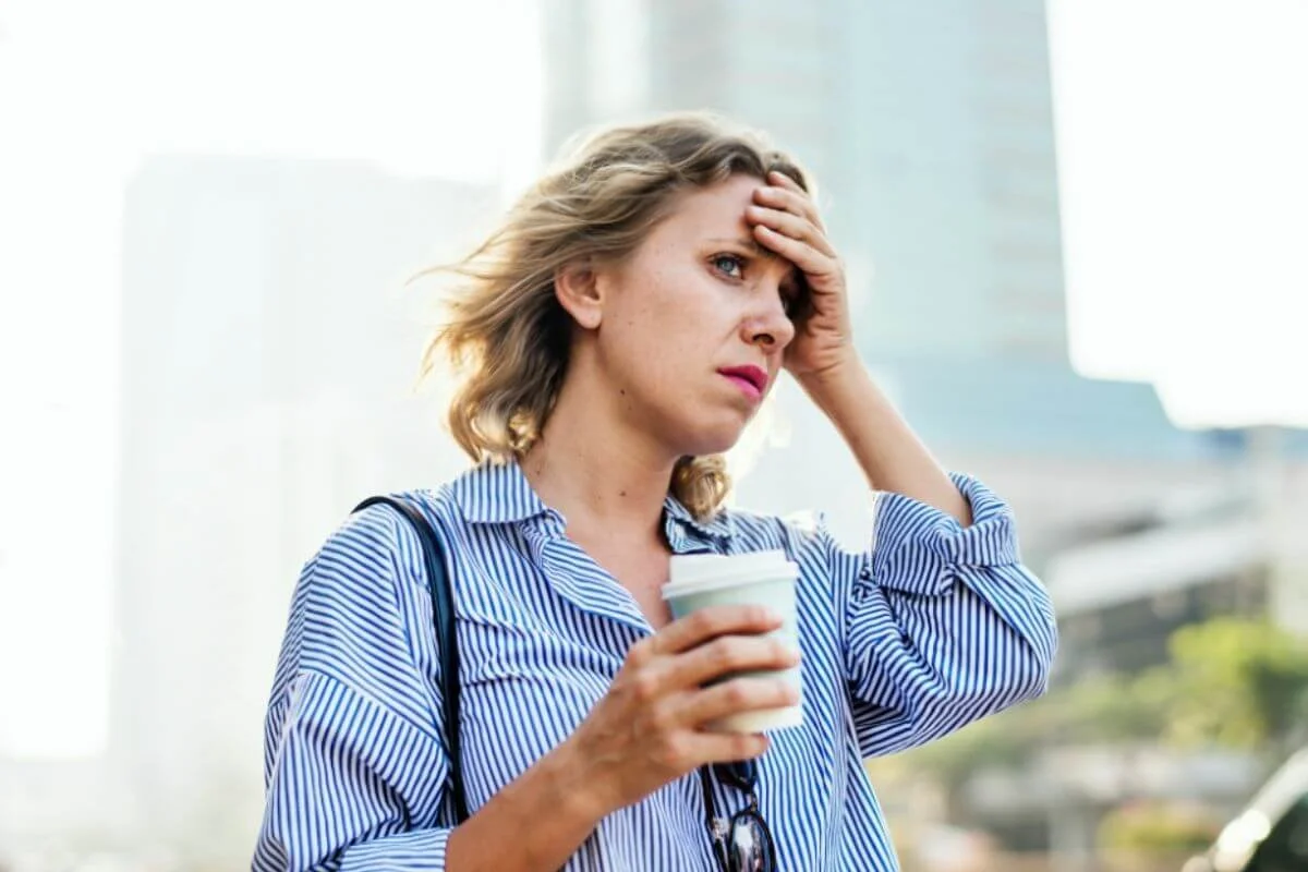 Woman holding a coffee with her other hands in her forehead