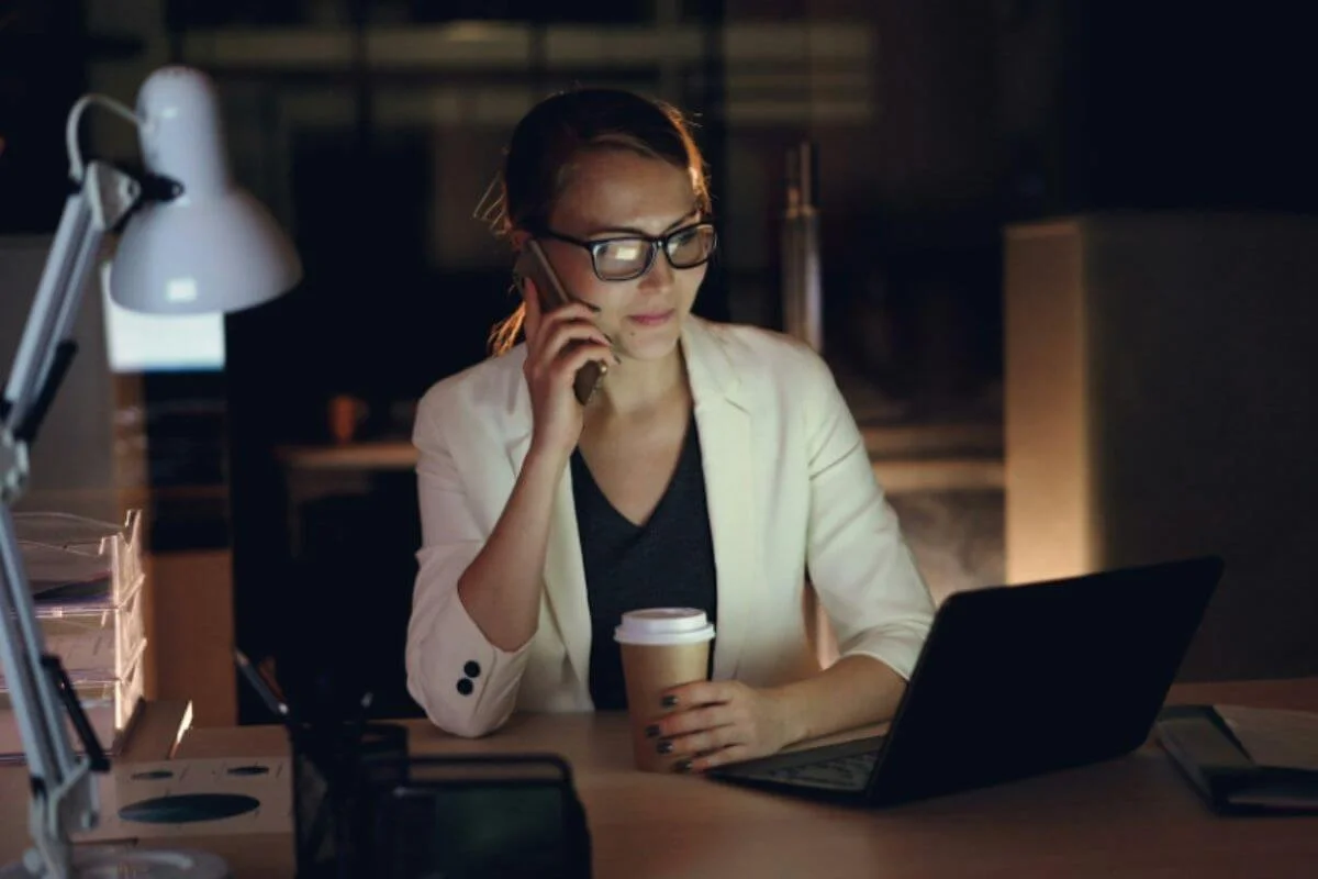 A woman on her phone while looking at the laptop