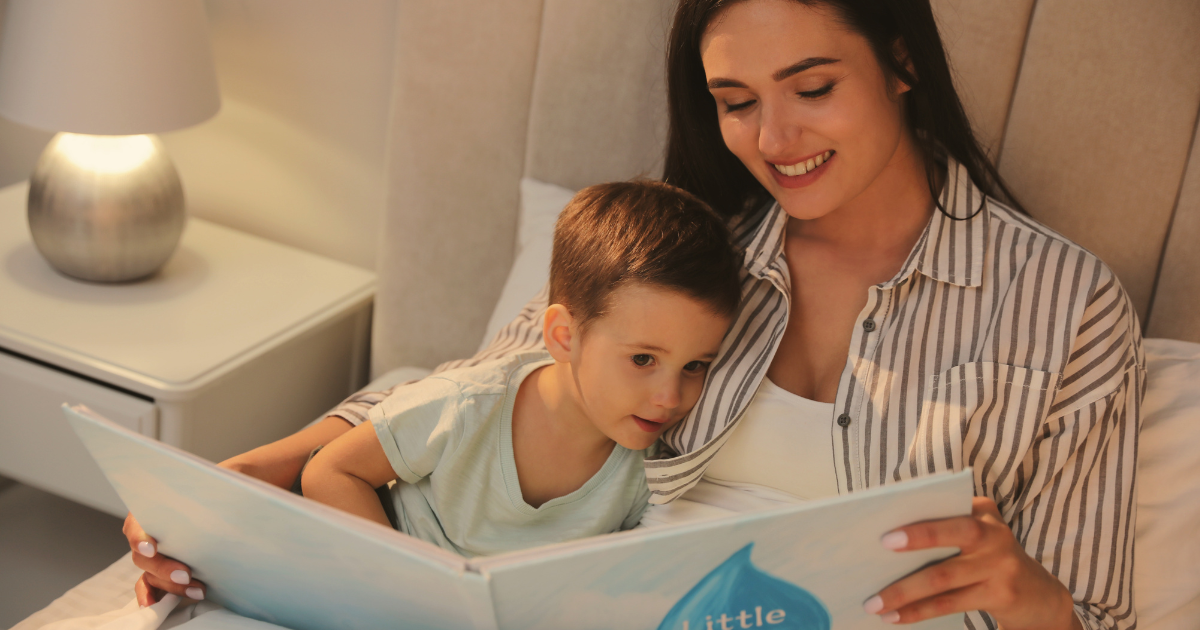 Mom reading a bedtime story to her toddler son while snuggled in bed with a lamp on