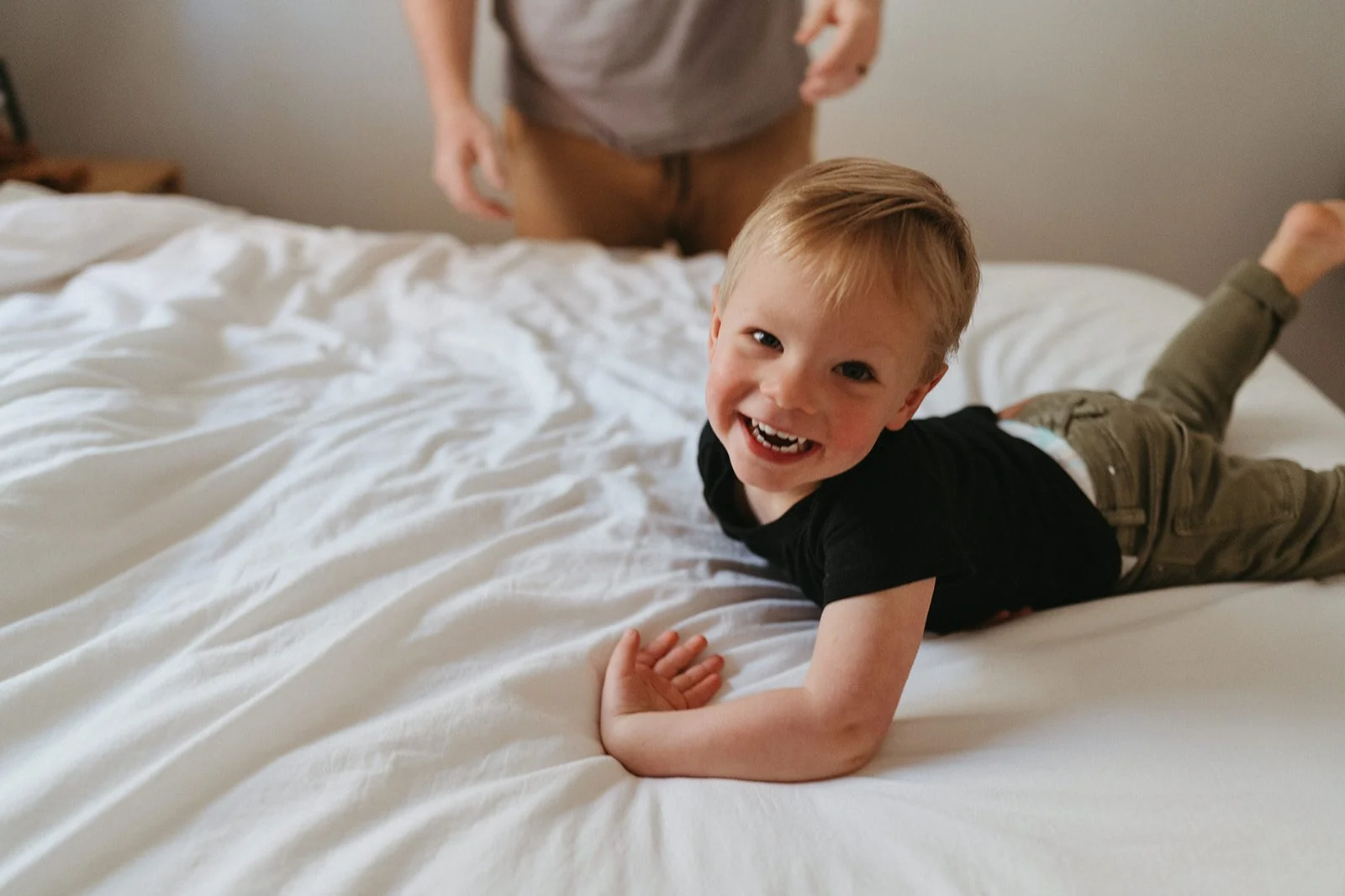 A happy toddler lays on a bed laughing, representing the playful side of the Ready, Set, Sleep Prep Plan approach.