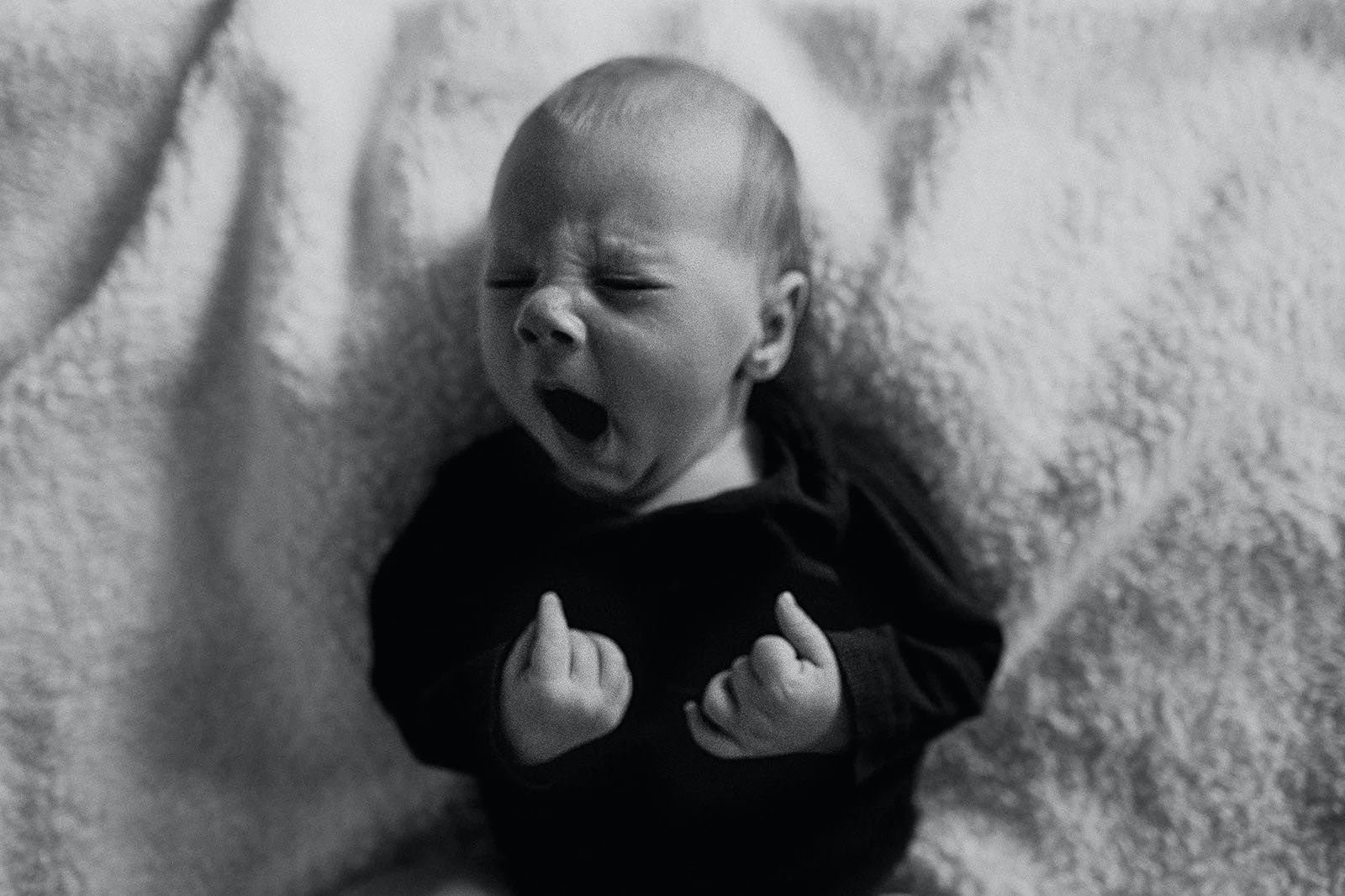 Overtired baby yawning with fists clenched, showing signs of infant sleep deprivation and need for a pediatric sleep consultant