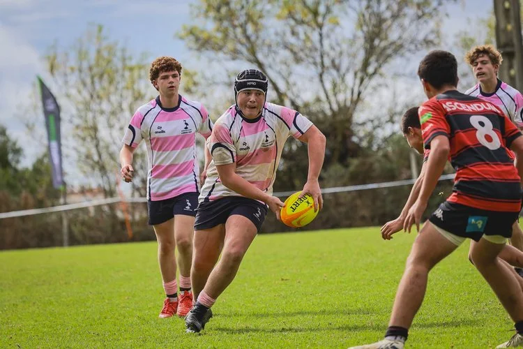 Youth rugby player running with the ball during a match at the Portugal Rugby Youth Festival Autumn Series, with defenders closing in.