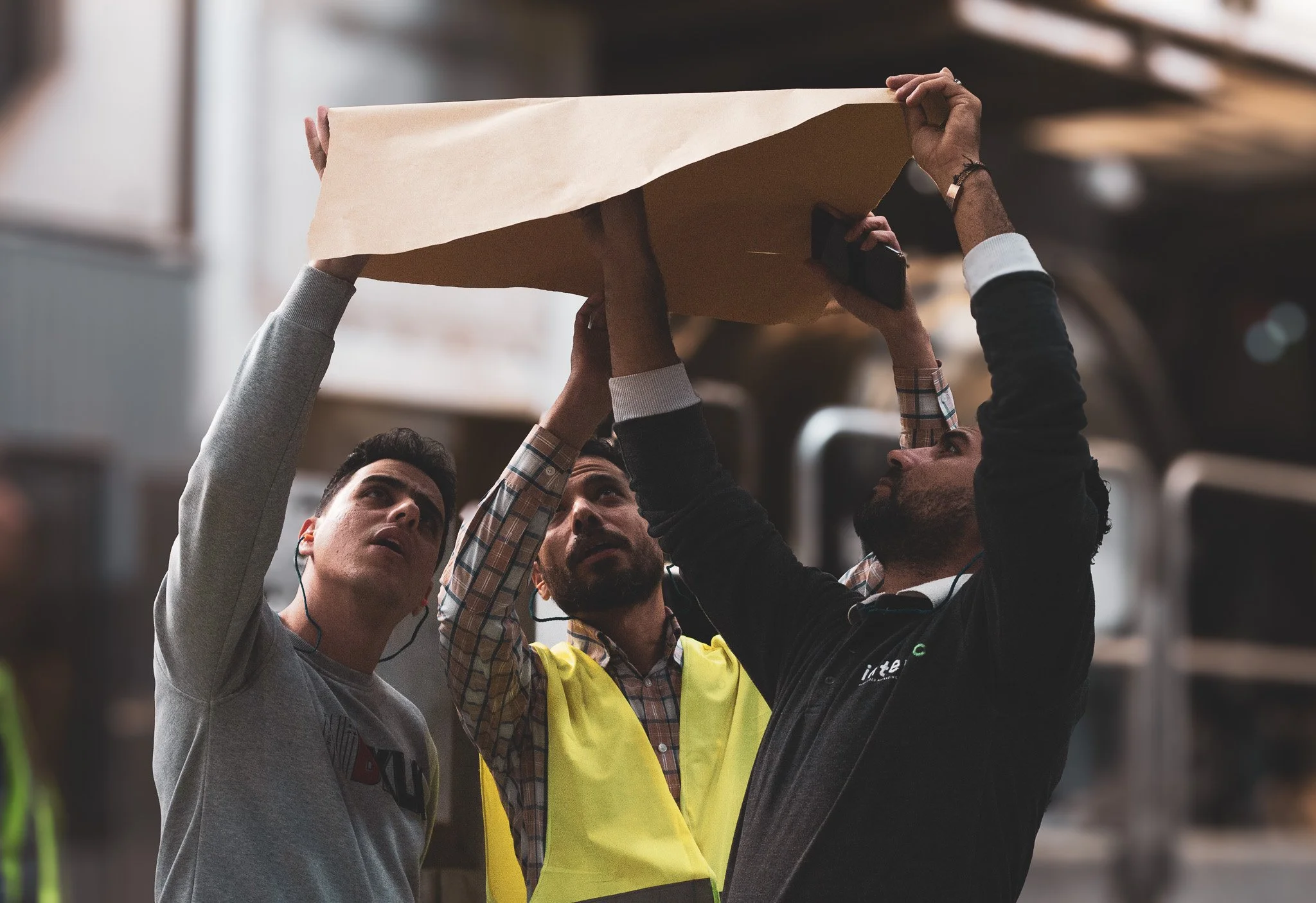Three men working together, inspecting or examining something overhead, in an indoor warehouse or industrial setting.