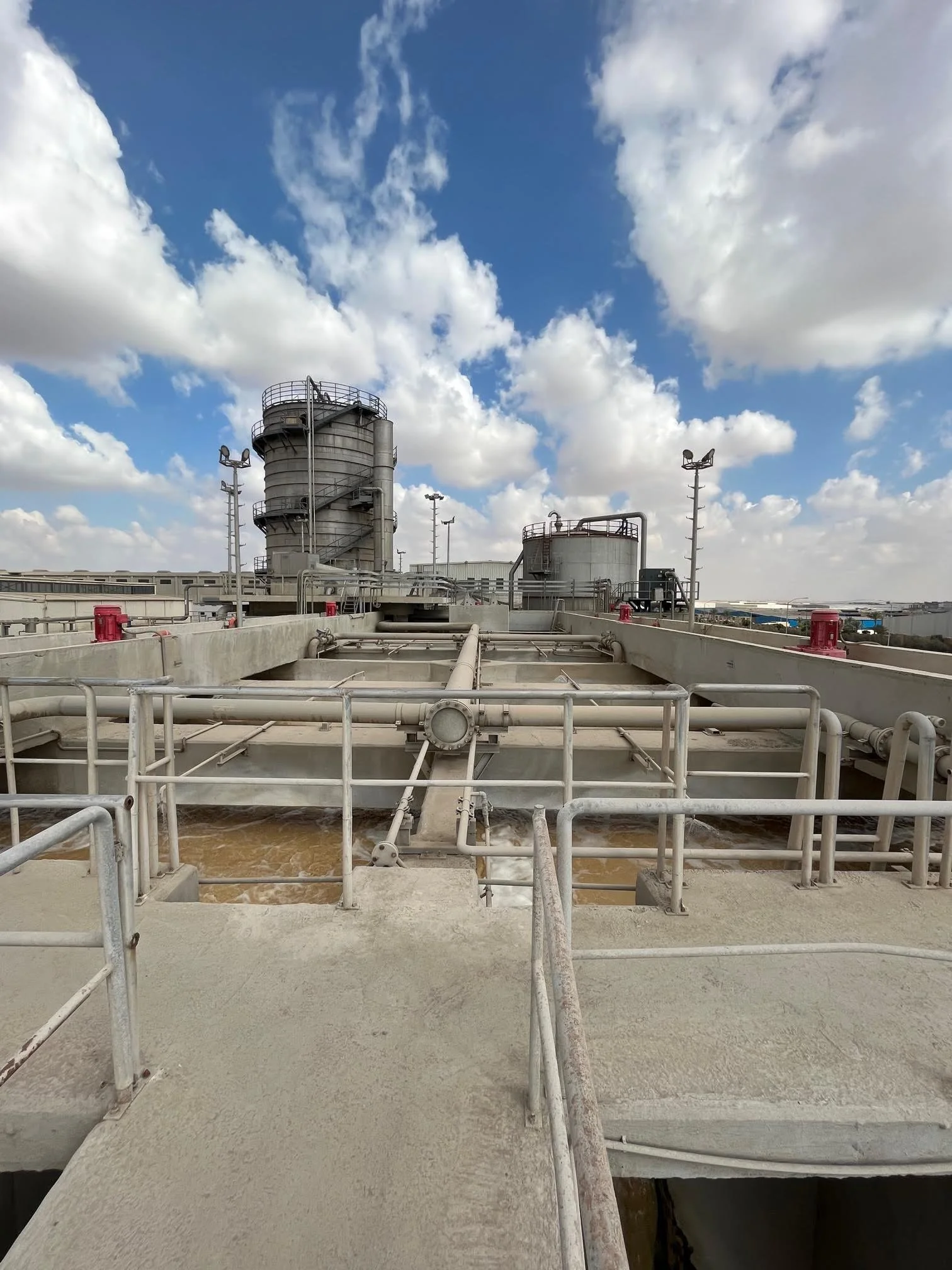 Industrial water treatment facility with tanks, pipes, and control structures under a partly cloudy sky.