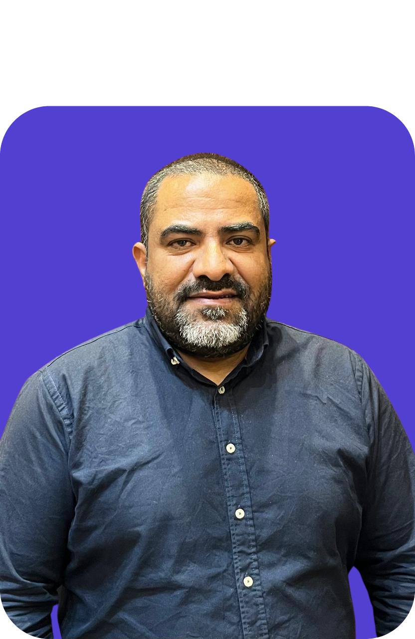 Portrait of a man with short dark hair and a beard, wearing a dark blue button-up shirt, against a purple background.
