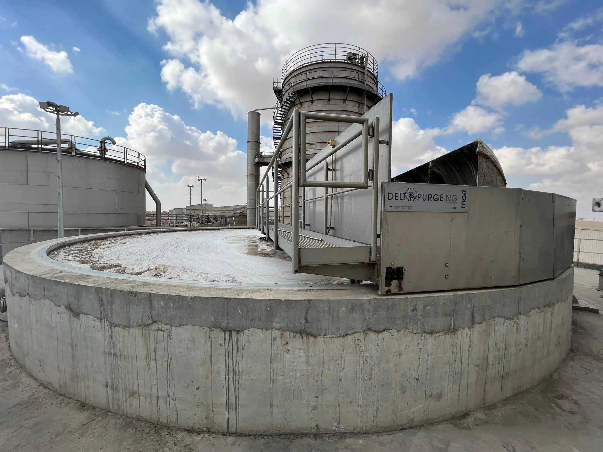 Industrial wastewater treatment tank with a rotating drum filter, on a rooftop under a cloudy sky.