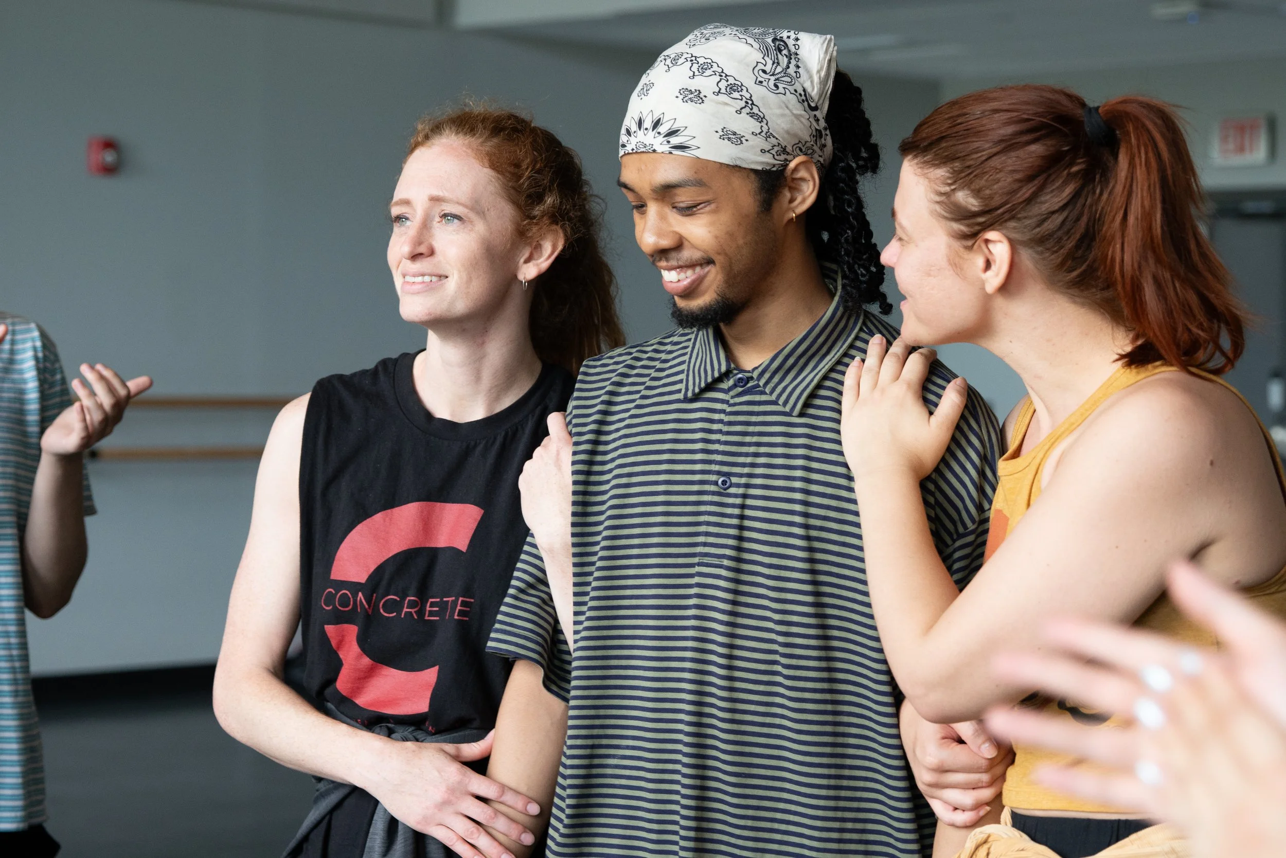Group of young adults smiling and chatting indoors, with one woman wearing a sleeveless shirt and another woman and man engaging in conversation.