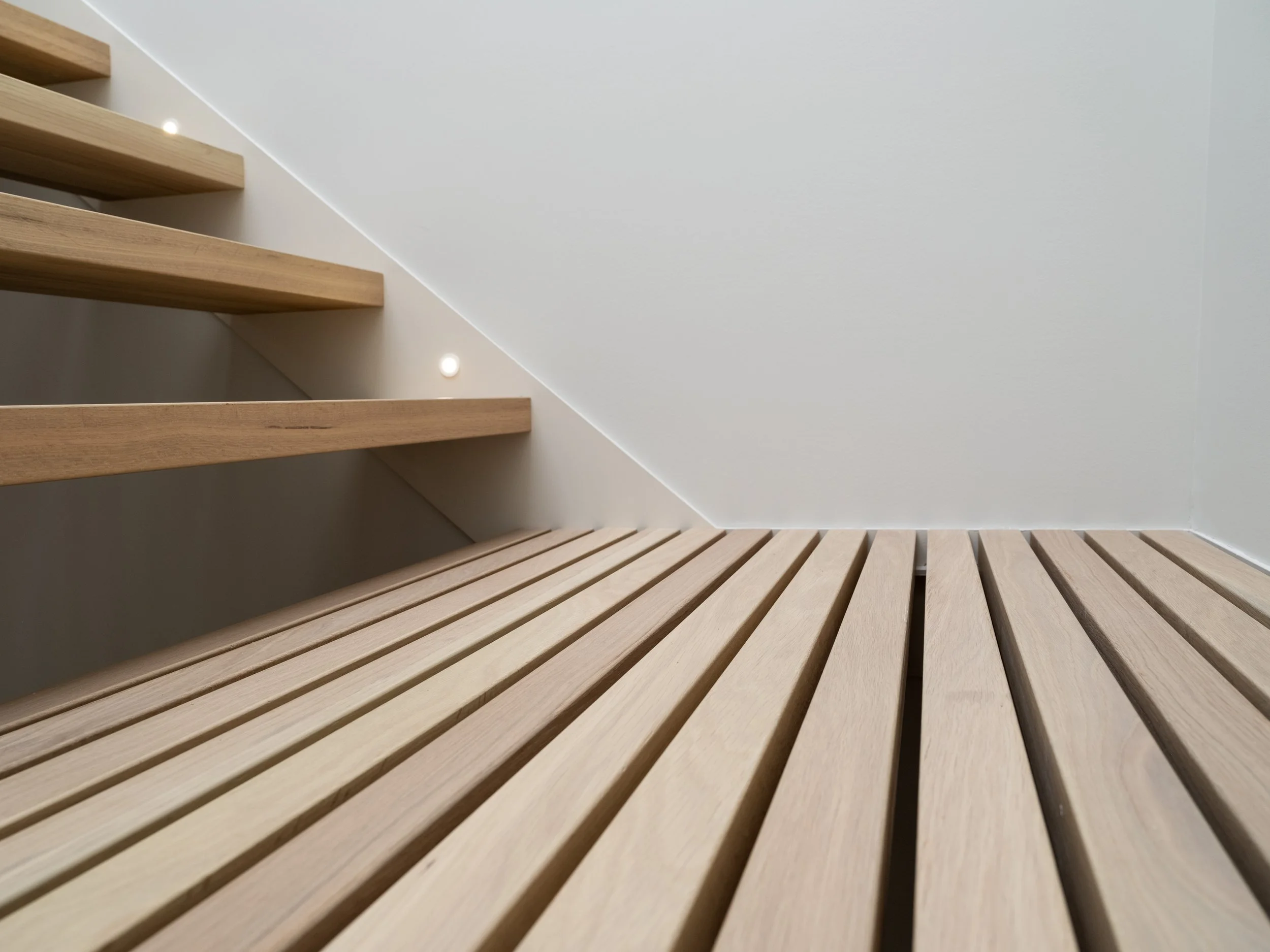 Vue rapprochée d'un palier en caillebotis de chêne blanc du projet signature Trafalgar, conçus pour alléger la structure et laisser circuler la lumière entre les étages.