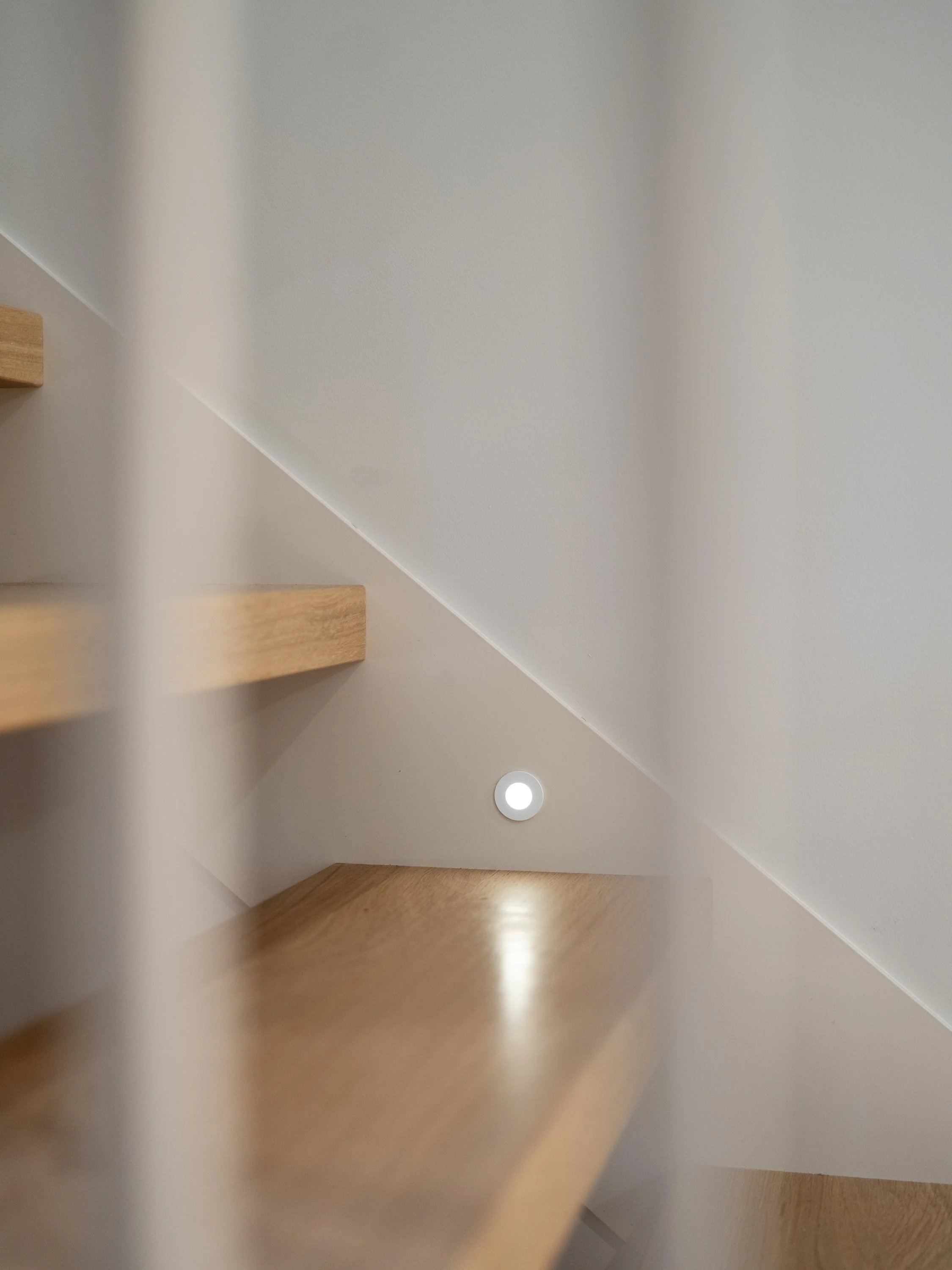 Escalier haut de gamme Trafalgar illuminé par un éclairage discret qui révèle la texture du chêne blanc et accentue la légèreté des marches ouvertes.
