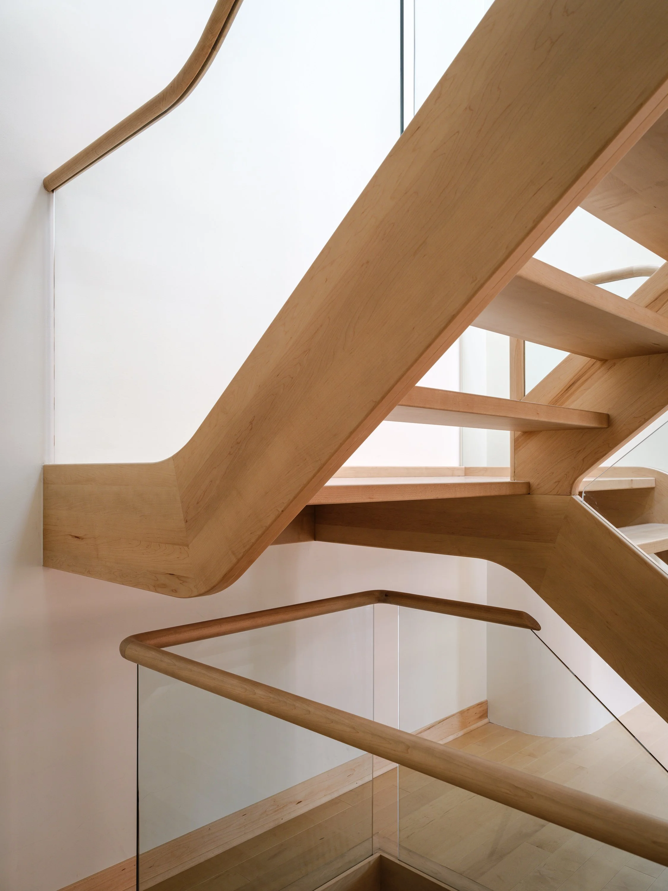 Détail de la structure en érable massif et des panneaux de verre intégrés à l’escalier sur mesure.