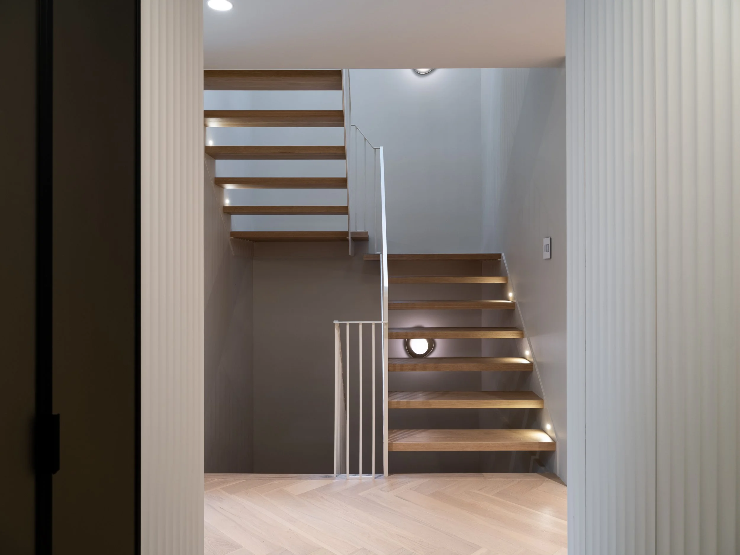 Escalier sur mesure avec marches ouvertes en chêne blanc massif d'une épaisseur de 2 pouces, limons fins en acier thermolaqué et garde-corps vertical continu.
