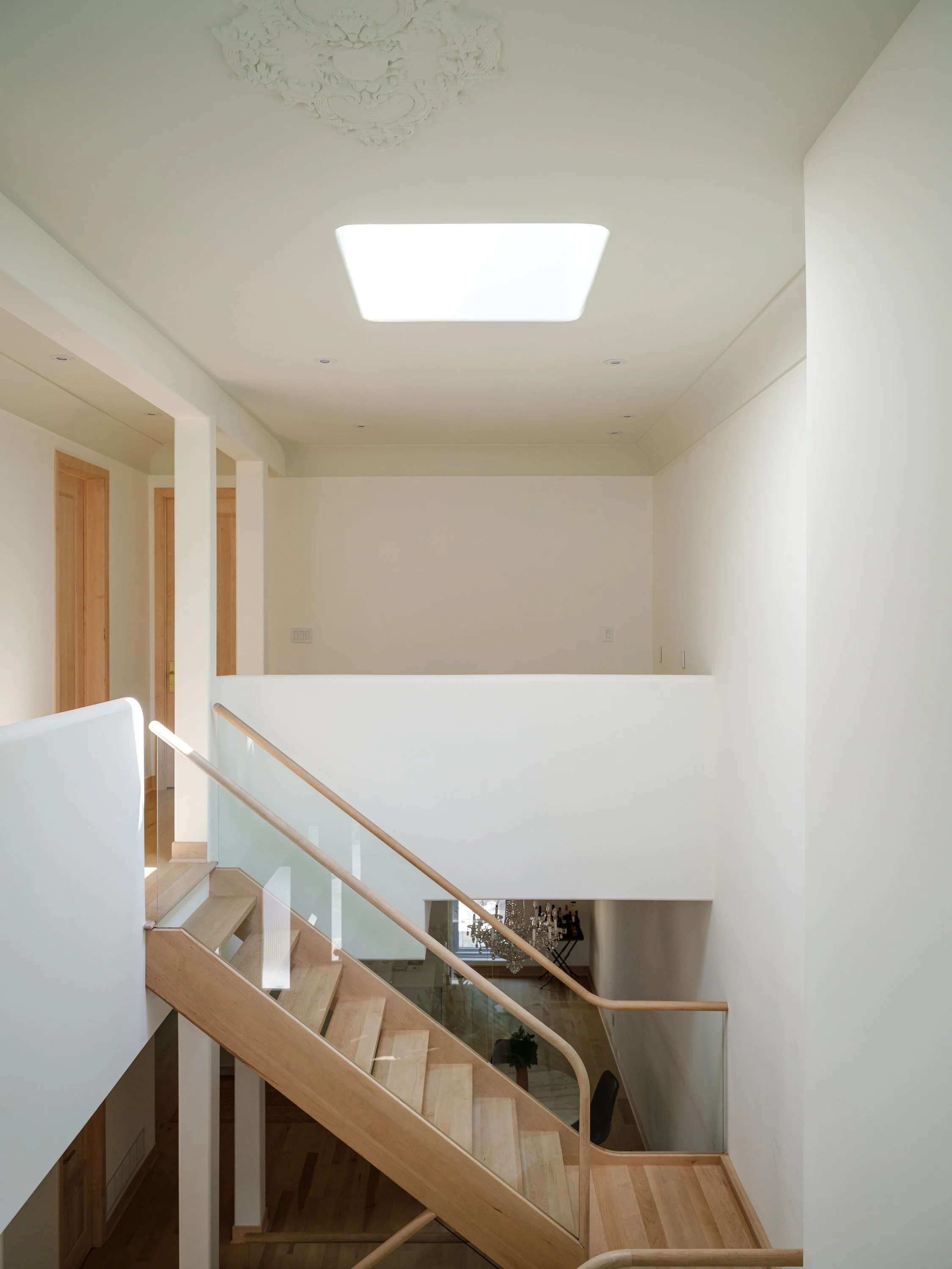 Palier lumineux avec garde-corps en verre et main courante continue en érable massif.