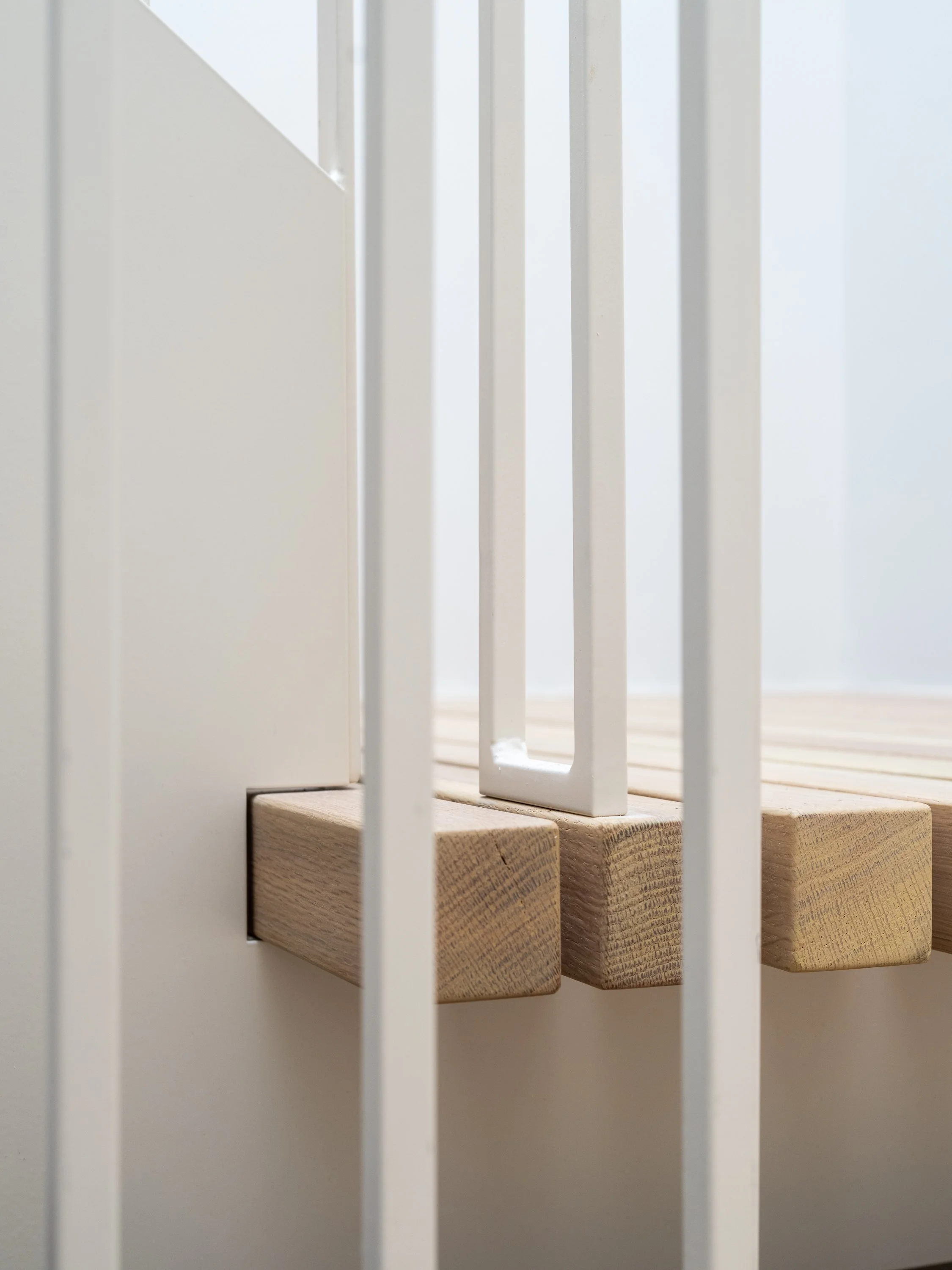 Détail de la rencontre du caillebotis en chêne blanc massif et du garde-corps géométrique en acier thermolaqué dans la conception contemporaine de l’escalier architectural du projet Signature Trafalgar.
