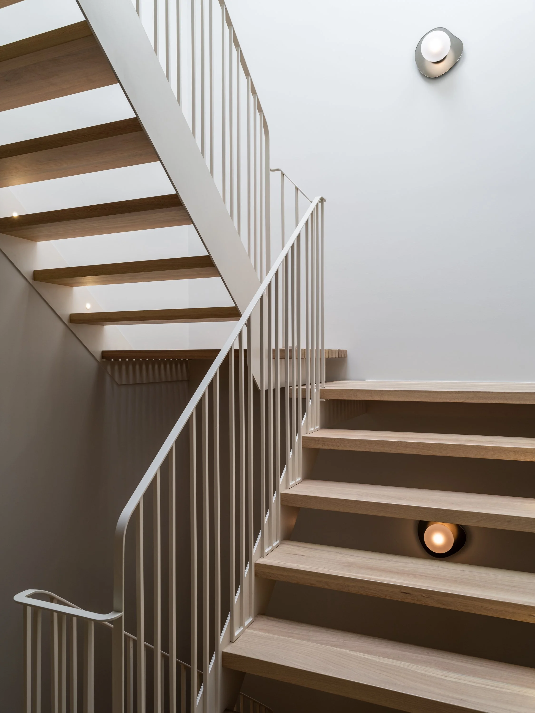 Vue de face de l’escalier sur mesure du projet Signature Trafalgar révélant la finesse de la structure d’acier et le rythme des marches en chêne blanc.