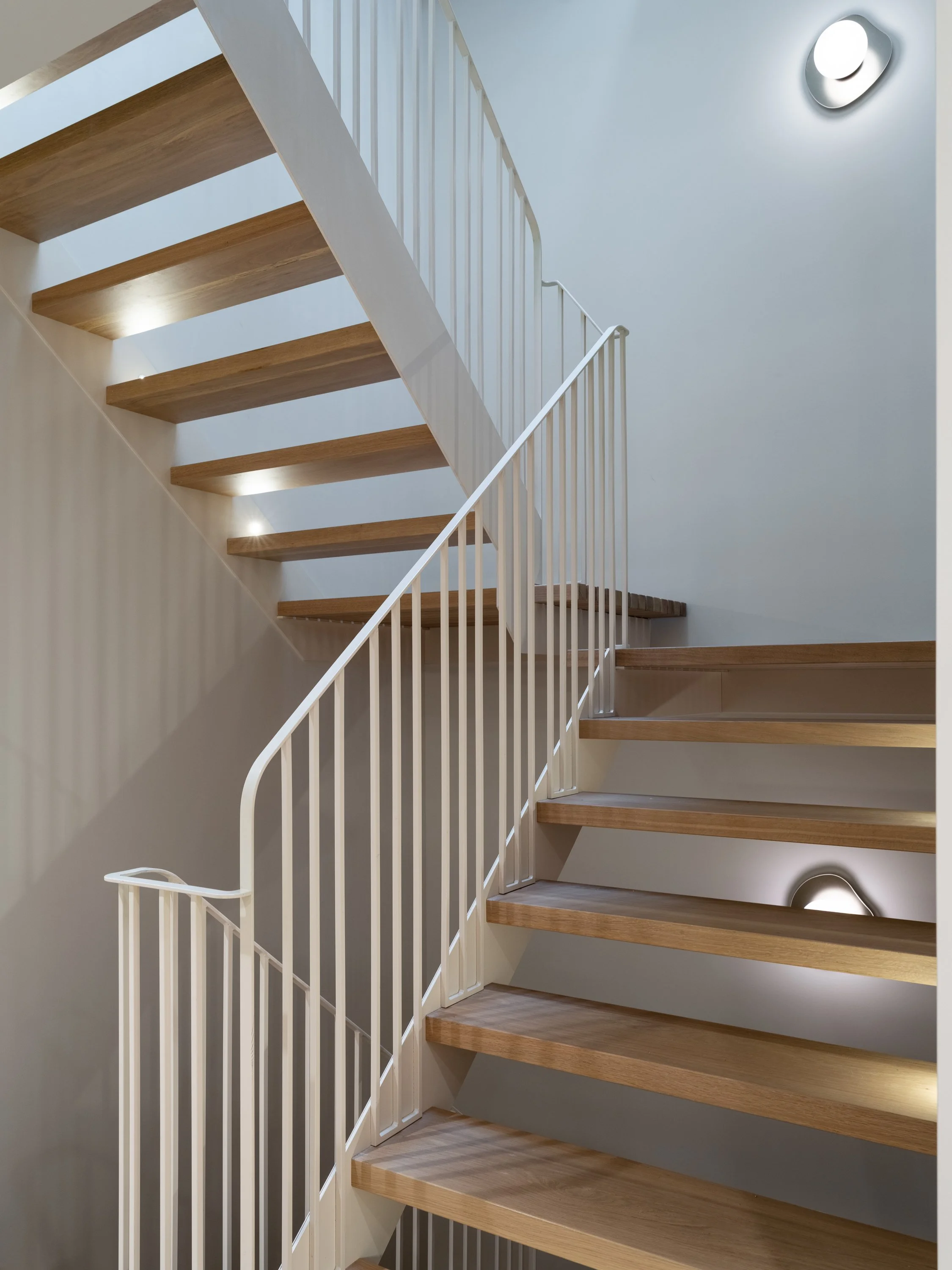 Escalier architectural du projet Signature Trafalgar en chêne blanc et acier thermolaqué, conçu sur mesure pour s’intégrer avec légèreté à l’architecture intérieure.