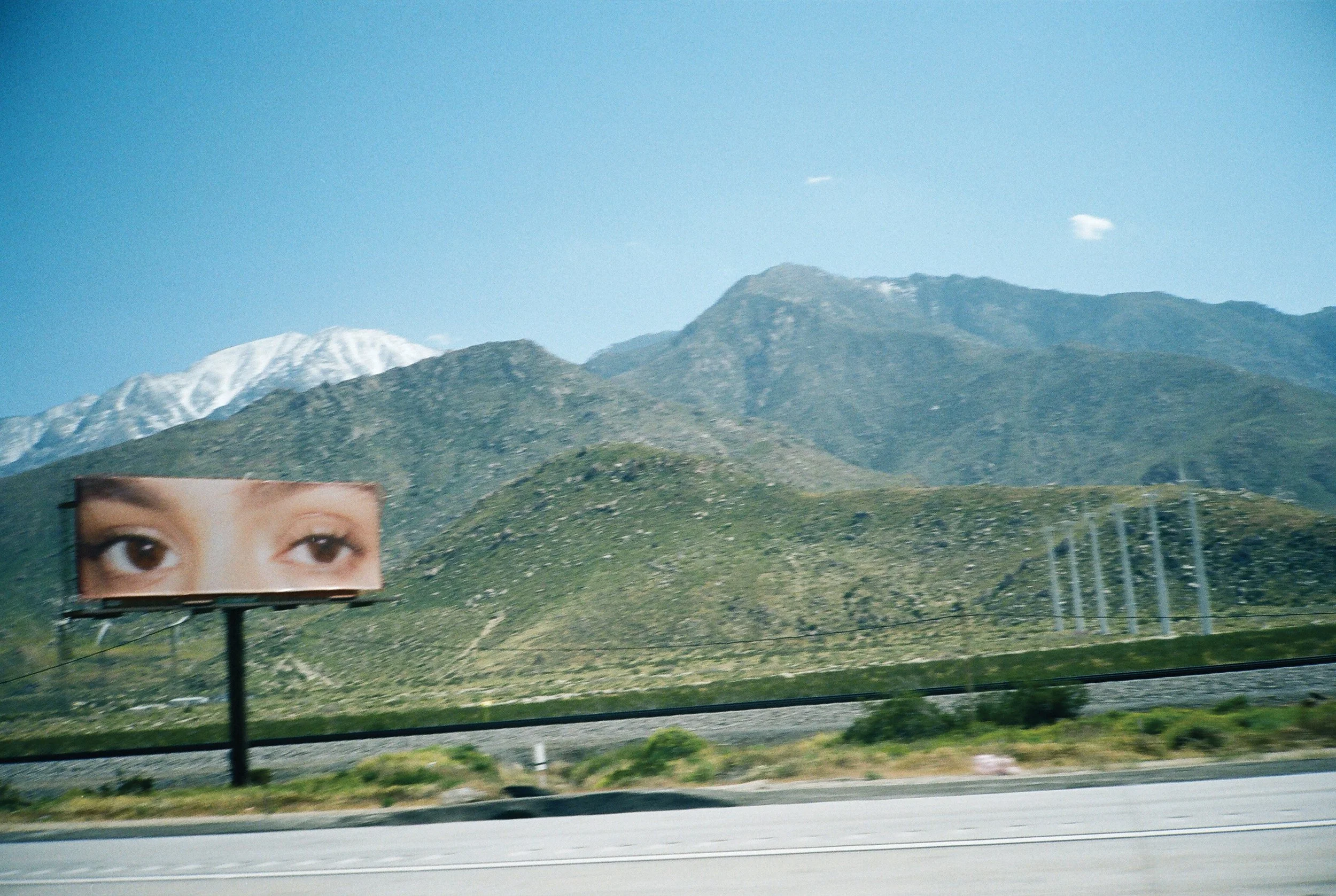 Billboard with a close-up of a person's eyes, set against a mountainous landscape with blue sky and snow-capped peaks.