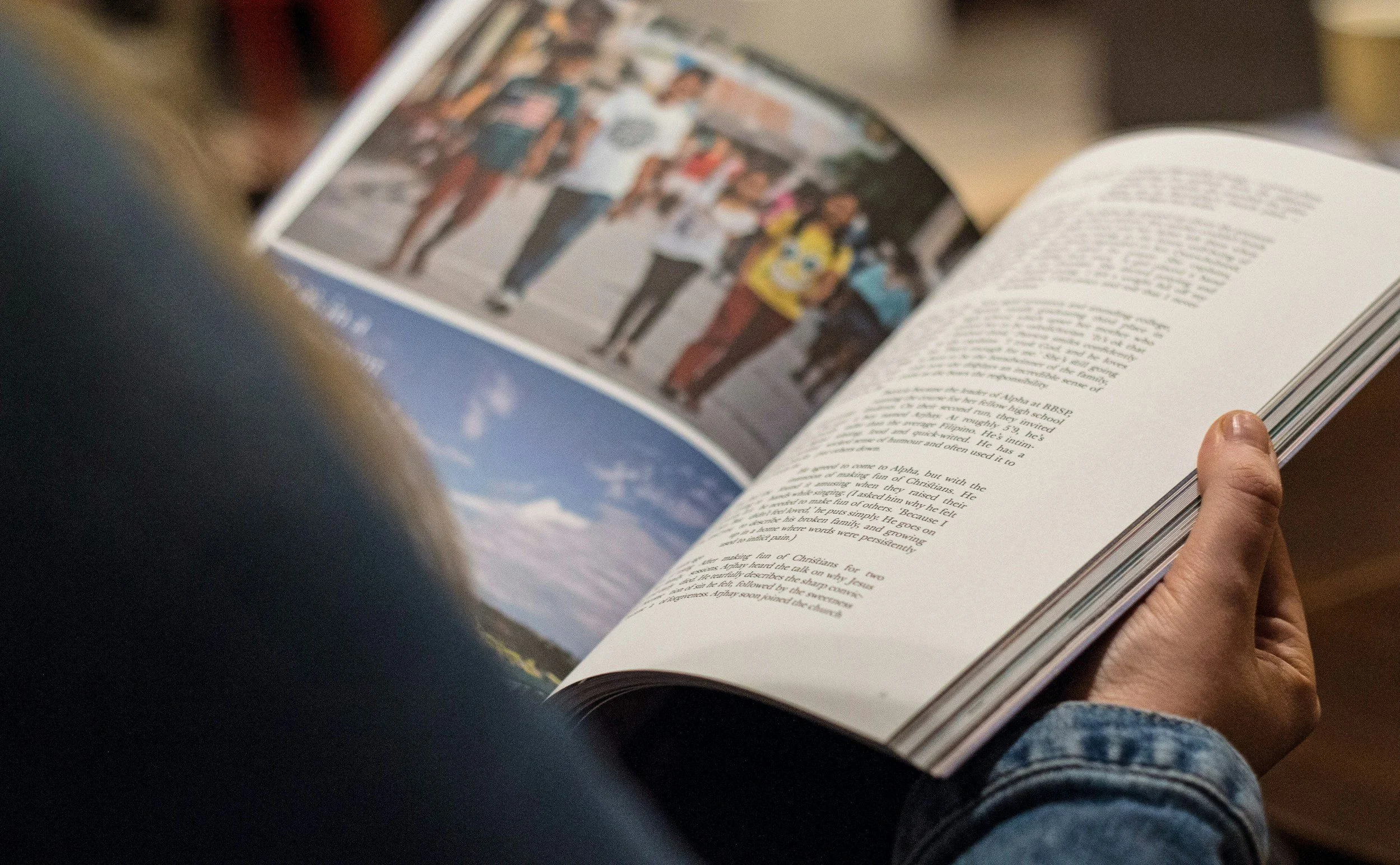 A person holding an open book with a photograph of people walking outdoors on one page and text on the other page.