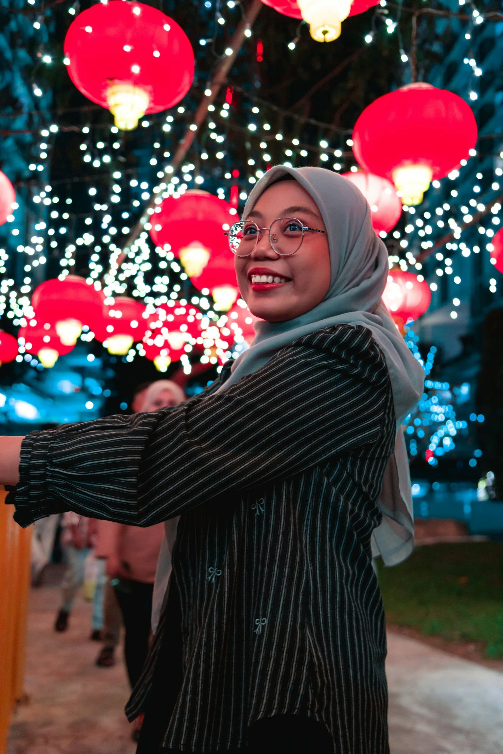 smiling woman with a hijab and glasses looking at lanterns