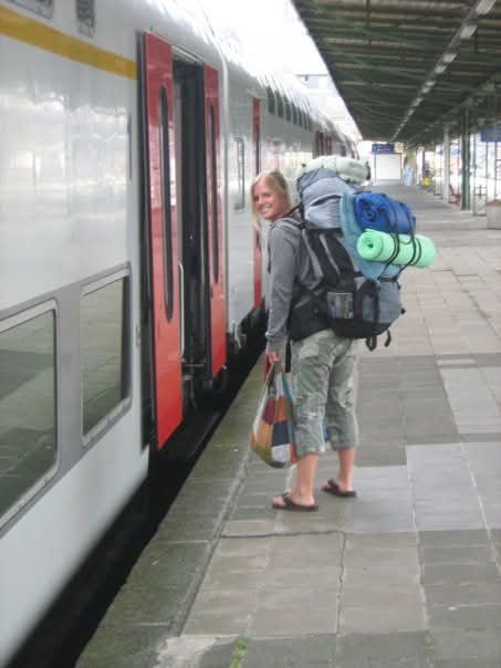 A woman with a large backpack and rolled-up sleeping mats boarding a train at the station.