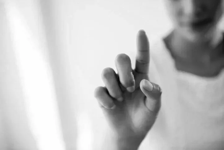 Close-up of a child's hand with the index finger pointing upward, in focus, on a blurred background.