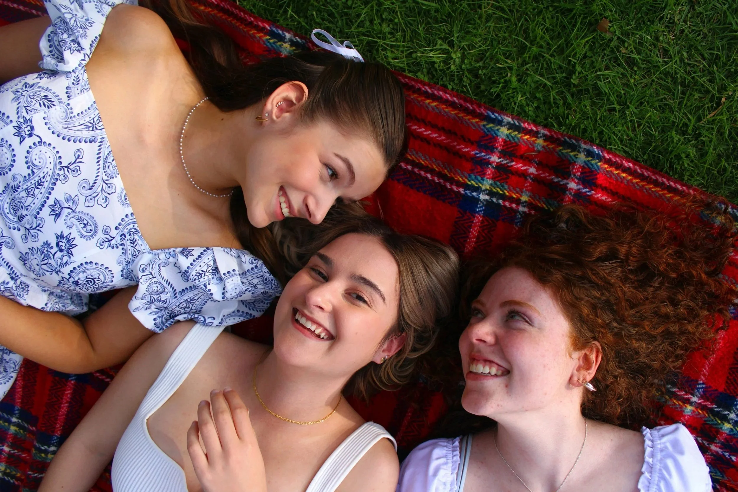 3 young people smiling and laying on the grass
