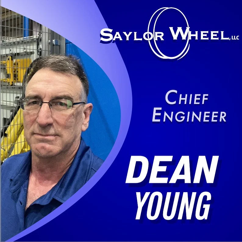 A portrait of Dean Young, a man with glasses and short dark hair, wearing a blue shirt, standing in front of a workshop. To the right, the image includes the logo for Saylor Wheel, LLC, and text indicating his role as Chief Engineer.