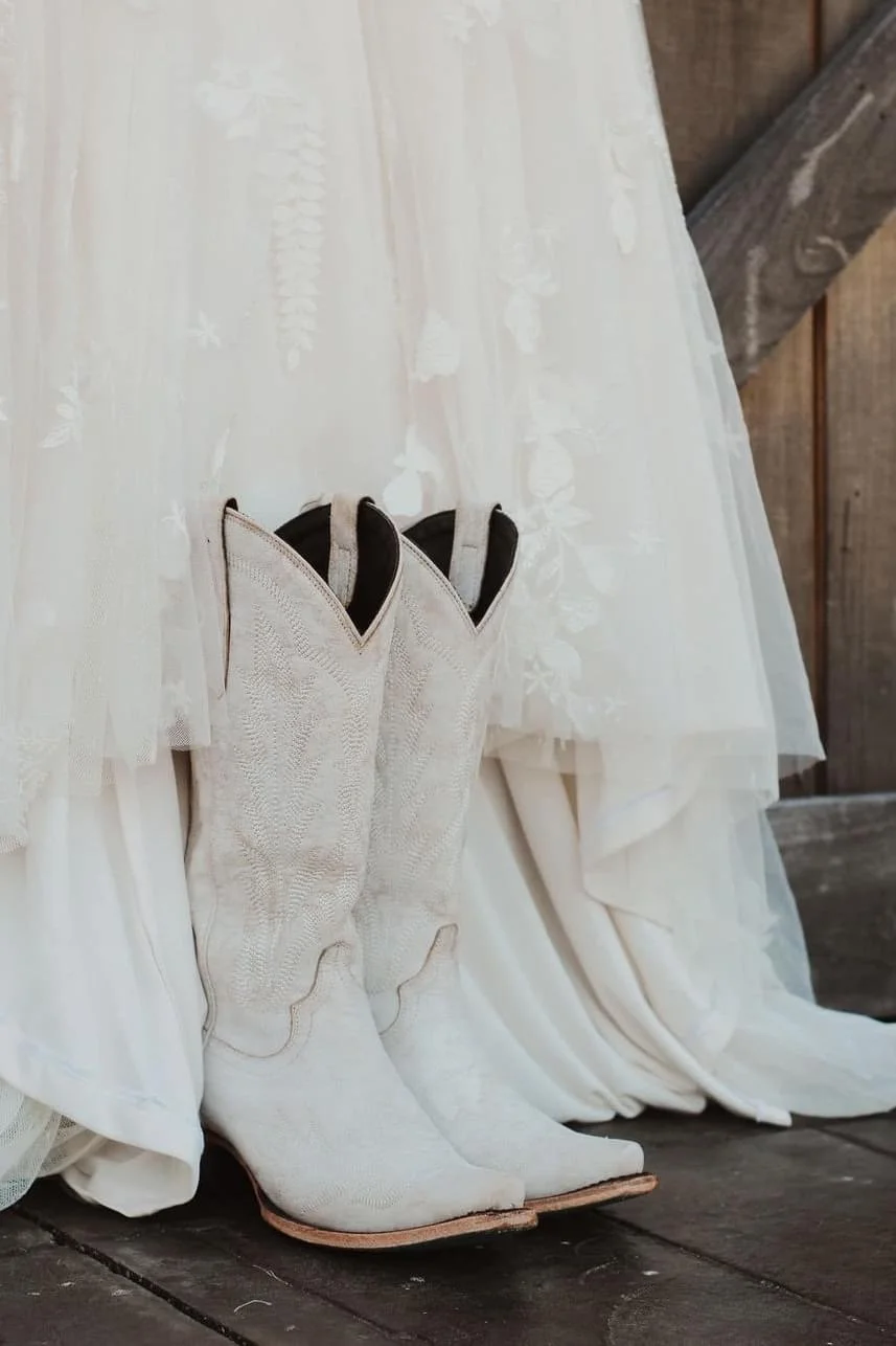 White cowboy boots in front of a lace wedding dress.