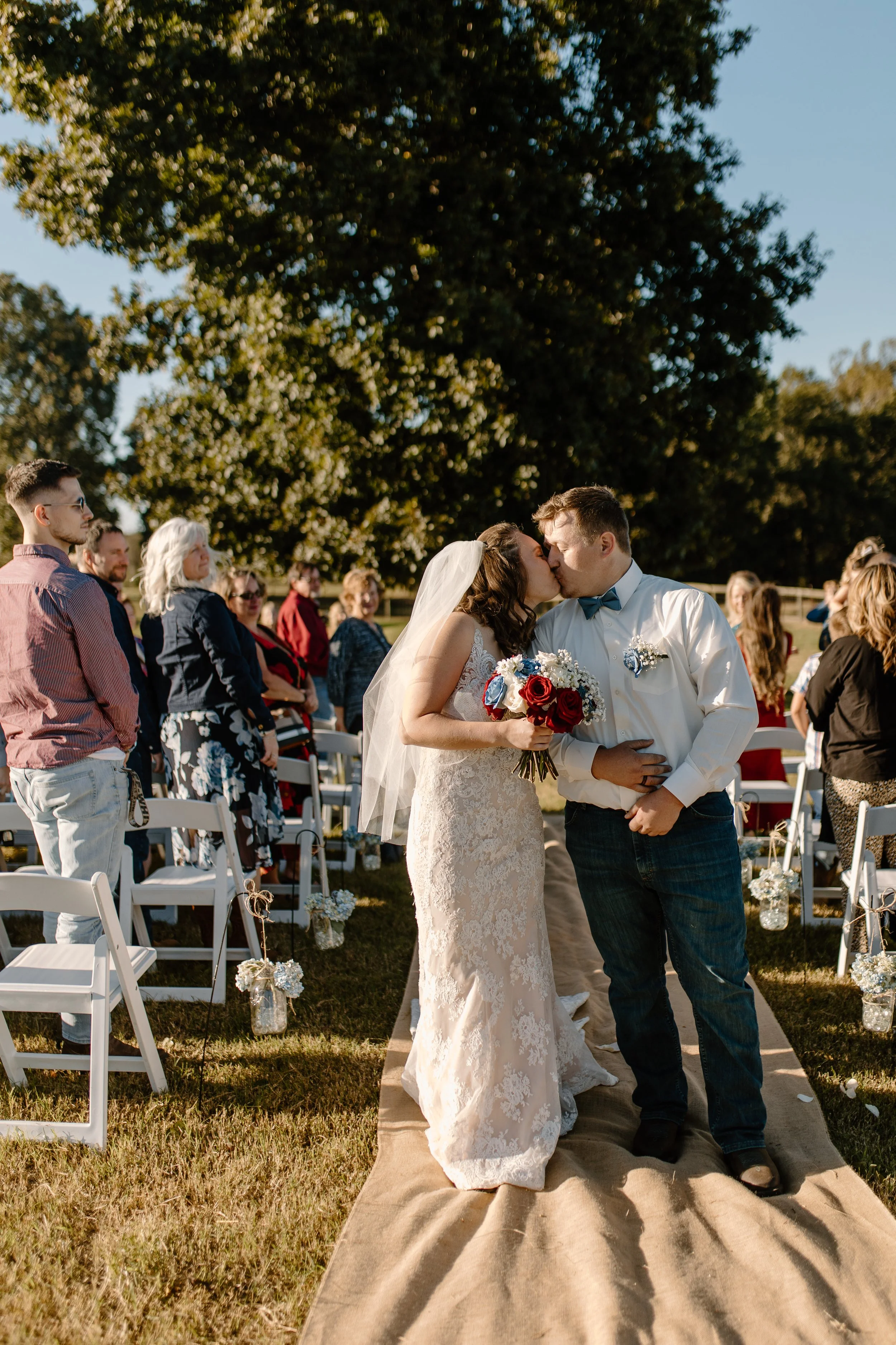 Bride and groom kissing during outdoor wedding ceremony with guests standing and watching.