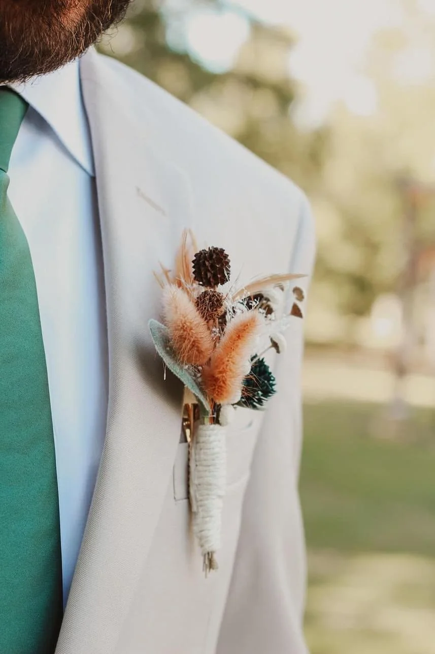 Close-up of a boutonniere with dried flowers on a beige suit, worn with a green tie.