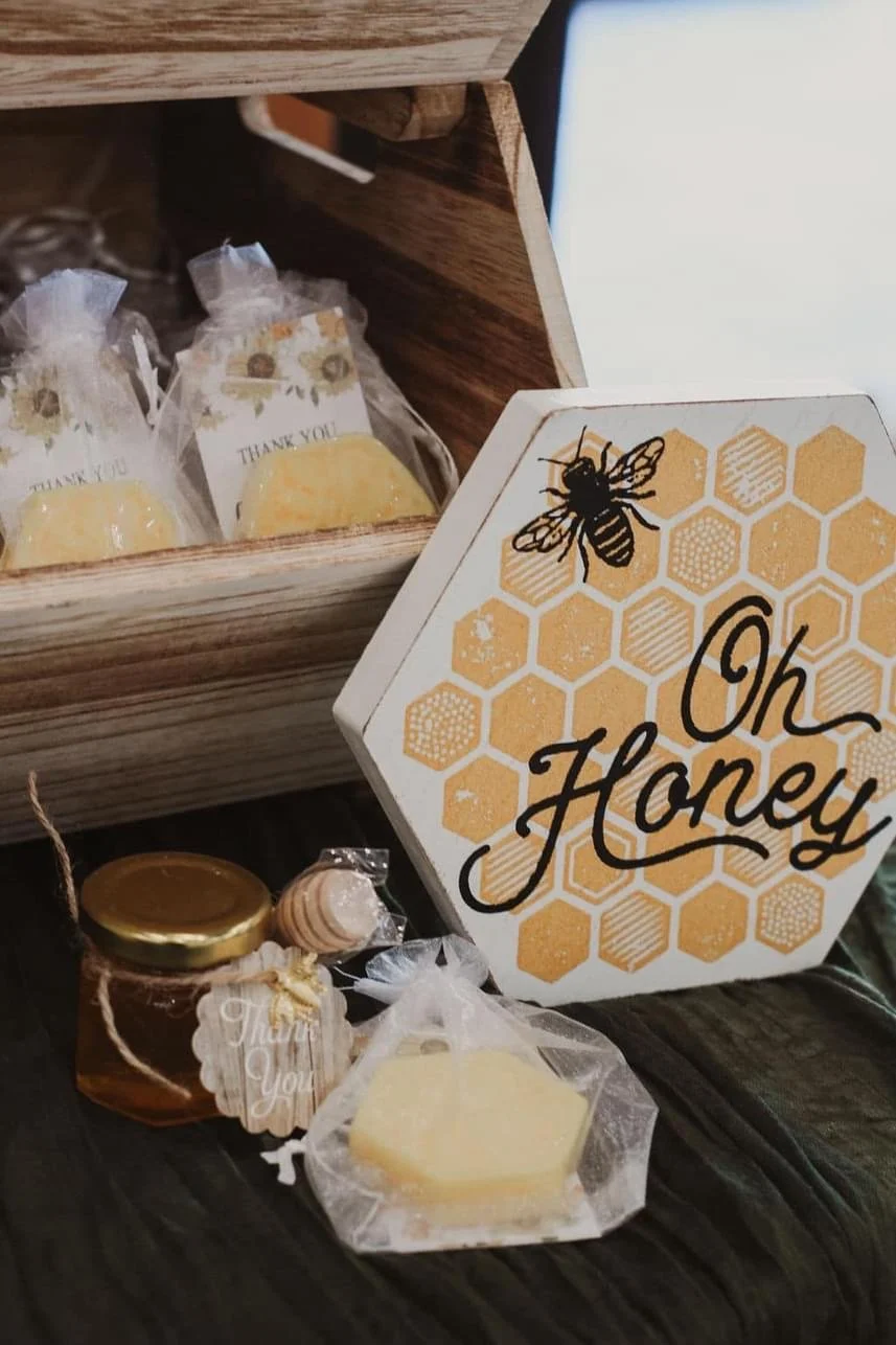 Decorative honey-themed display with "Oh Honey" sign, small jar of honey, decorative honey dipper, and honeycomb-shaped soap in bag.