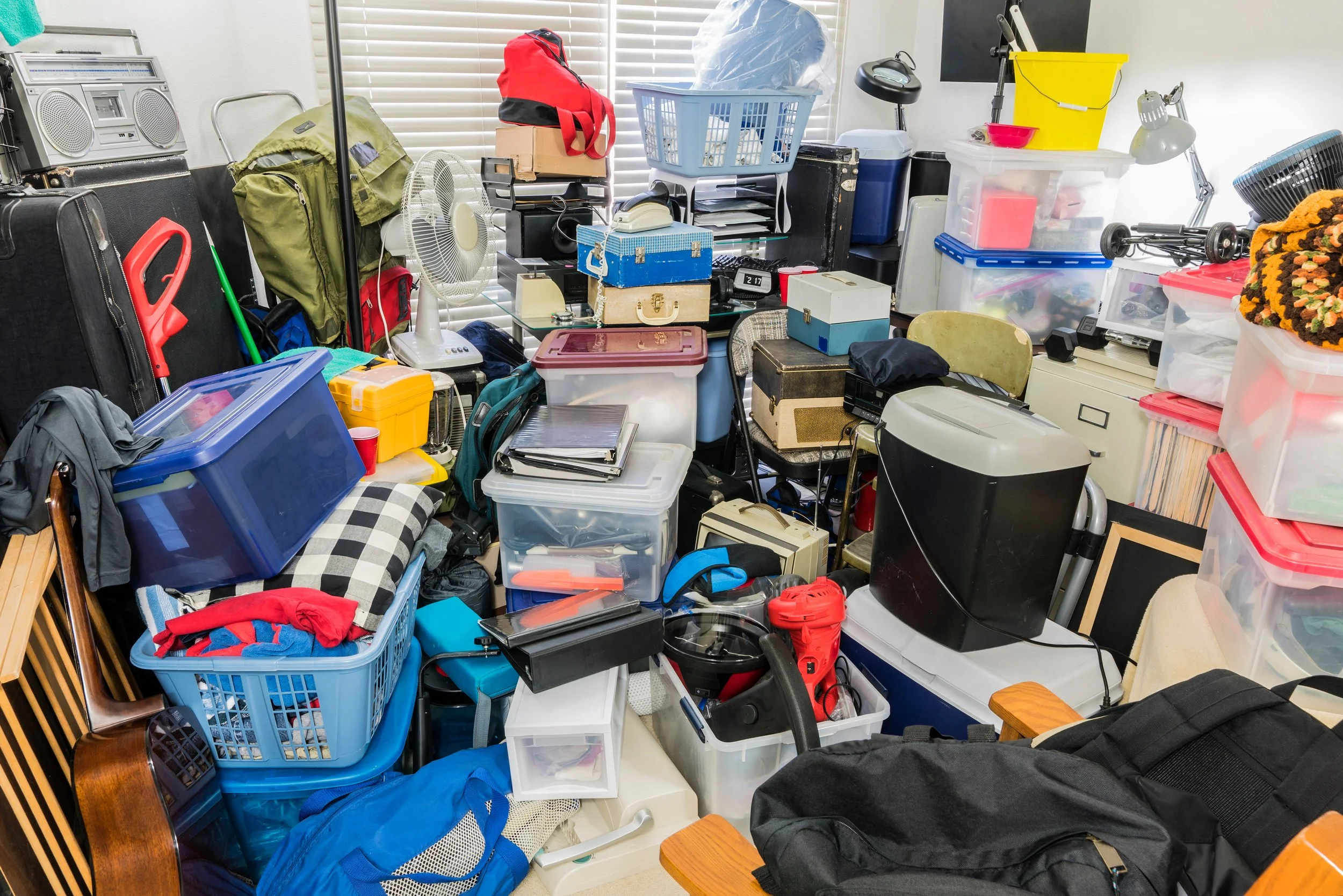 A cluttered room filled with various storage bins, suitcases, boxes, backpacks, and miscellaneous items.