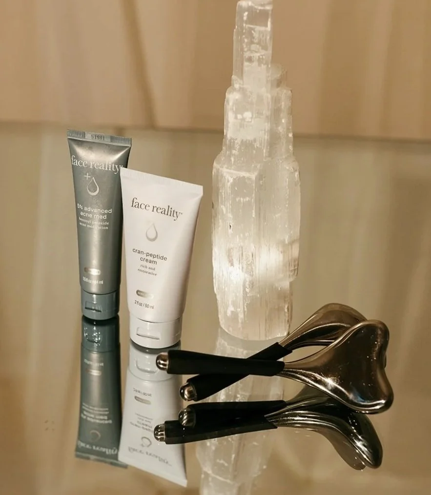 Two tubes of Face Reality skincare, a unique ice sculpture, and three metallic massage tools on a reflective surface.
