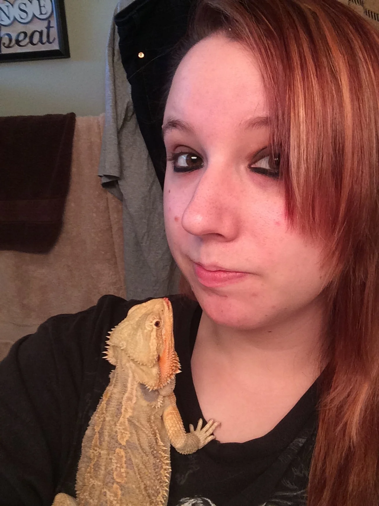 A young woman with reddish-brown hair taking a selfie with a bearded dragon lizard resting on her shoulder.