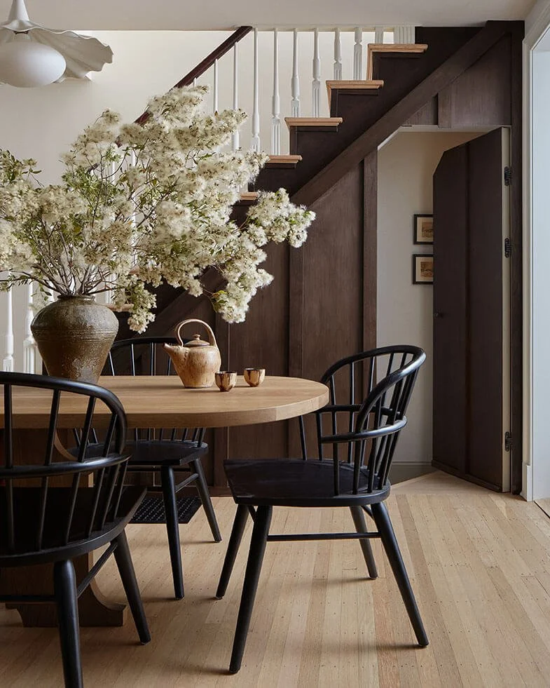Round dining table and black Windsor chairs by a walnut-paneled staircase in a Philadelphia home by Vestige Home