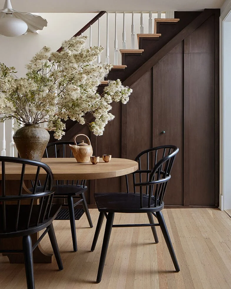 Dining area with a round oak table and black Windsor chairs beside walnut staircase paneling, by Vestige Home Philadelphia