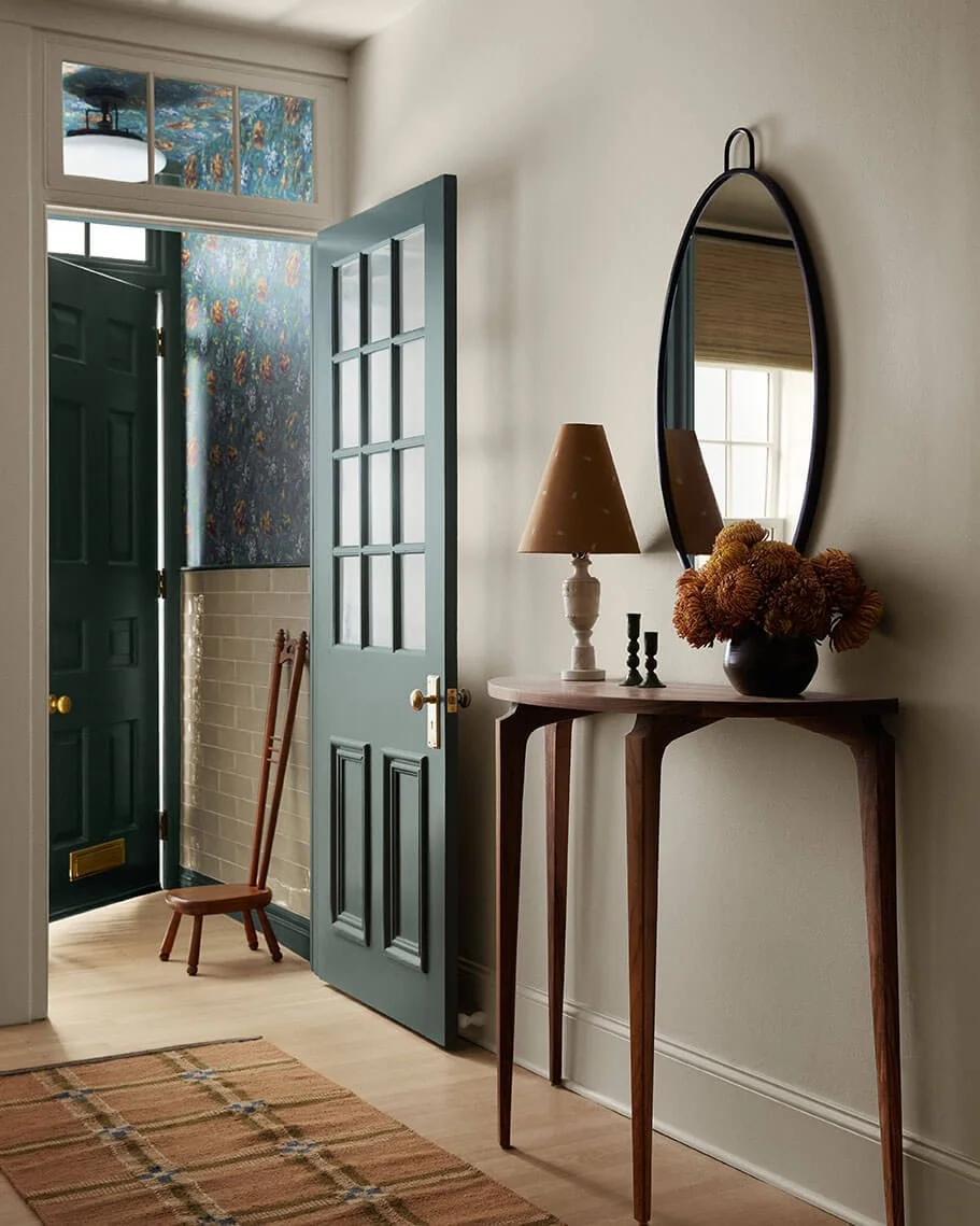 Entryway in a Philadelphia rowhouse by Vestige Home with floral wallpaper, a teal door, walnut console table and oval mirror.
