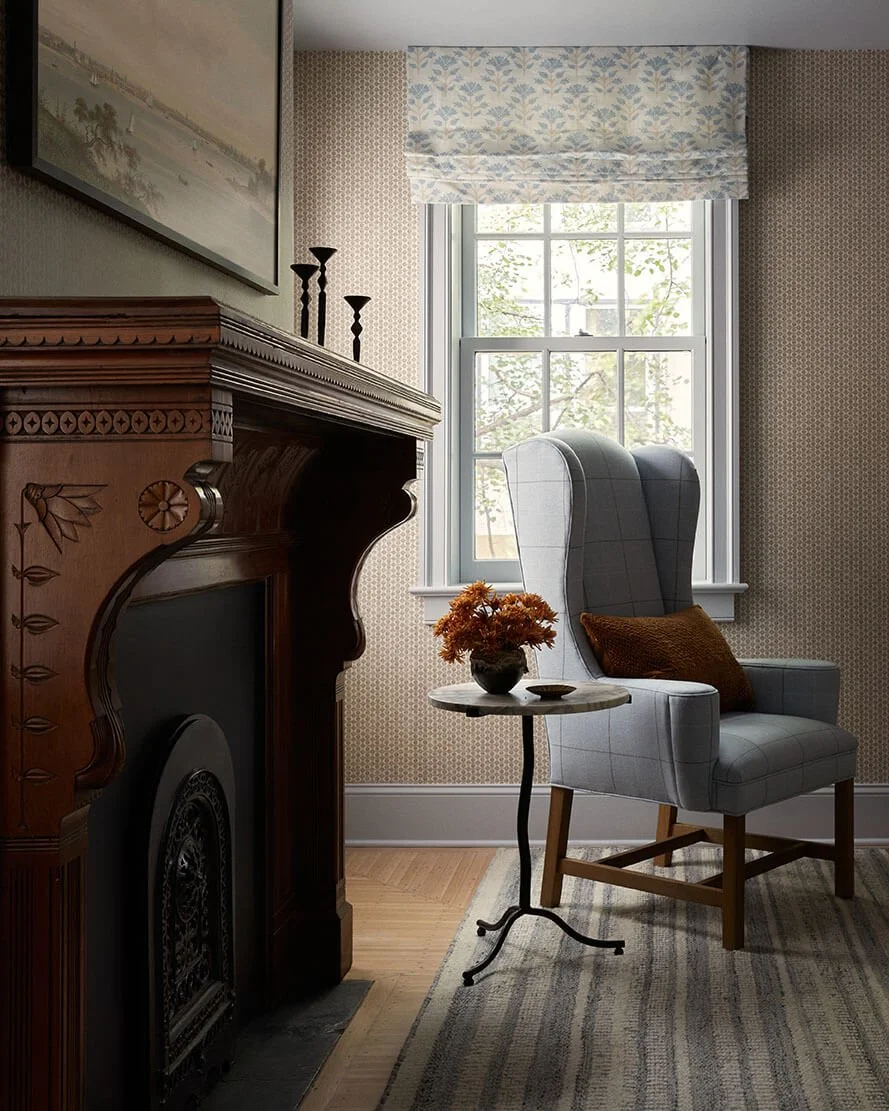 Antique carved wood fireplace mantel and a plaid wingback chair in a Vestige Home Philadelphia primary bedroom