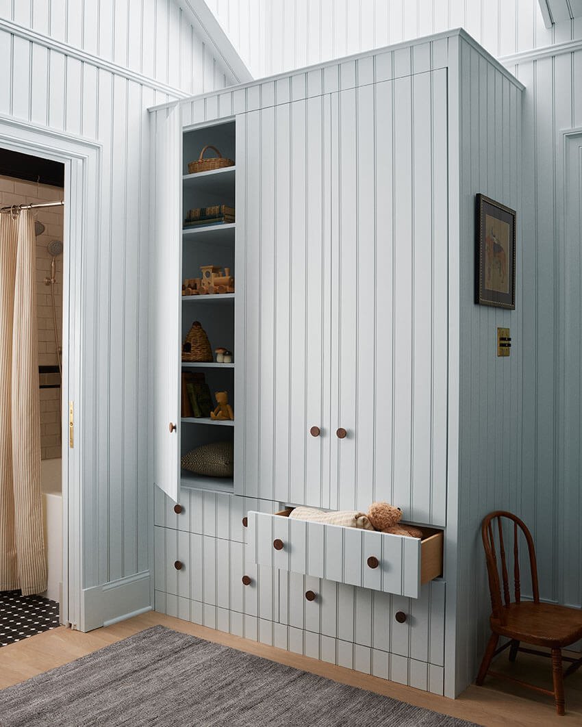 Light blue beadboard wardrobe with open shelving and wooden toys in a child's bedroom by Vestige Home Philadelphia