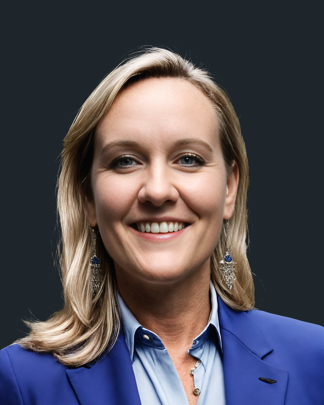 A woman with blonde hair wearing a blue blazer and earrings, smiling against a black background.